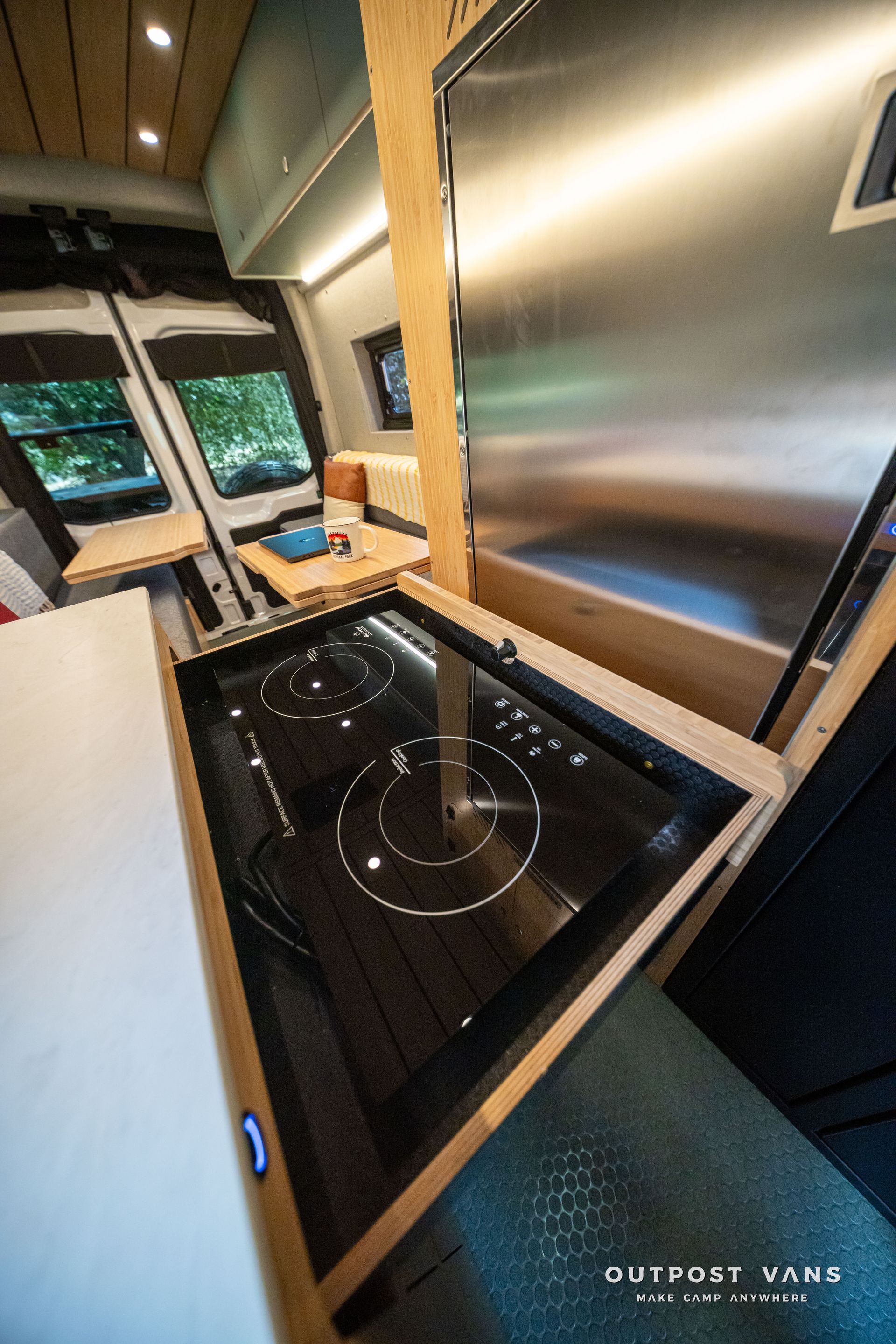 Tiny cabin kitchenette with glossy black induction cooktop and stainless counter by windows