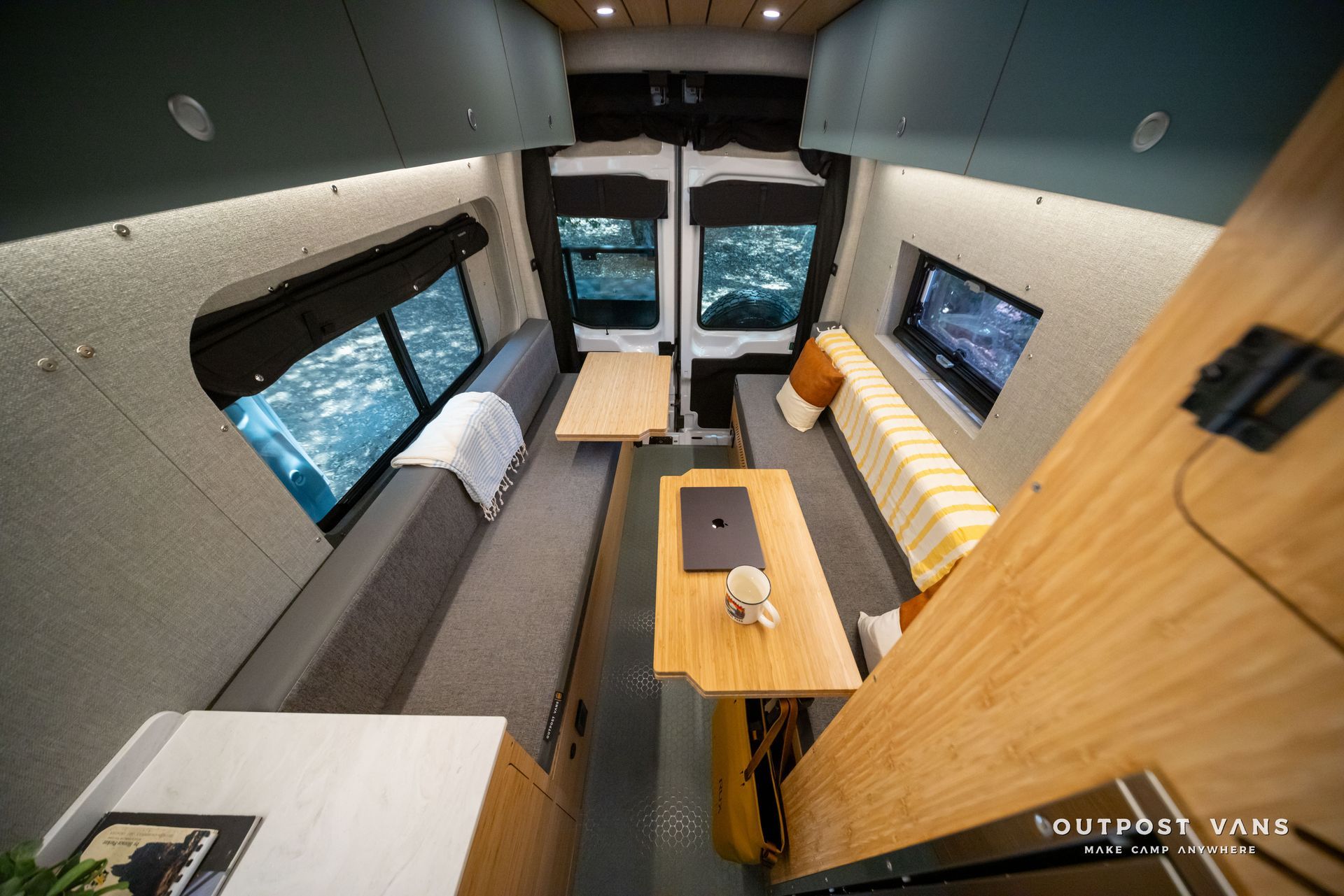Compact camper van interior with twin benches, wooden table, and skylight windows.