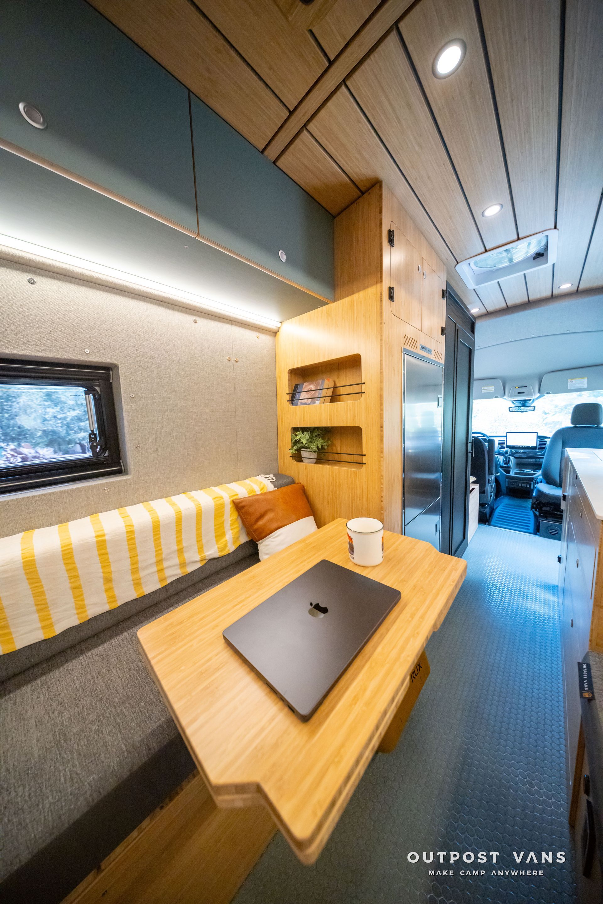 Compact wood-paneled camper interior with desk, sofa, and skylight leading to a bright front seating area