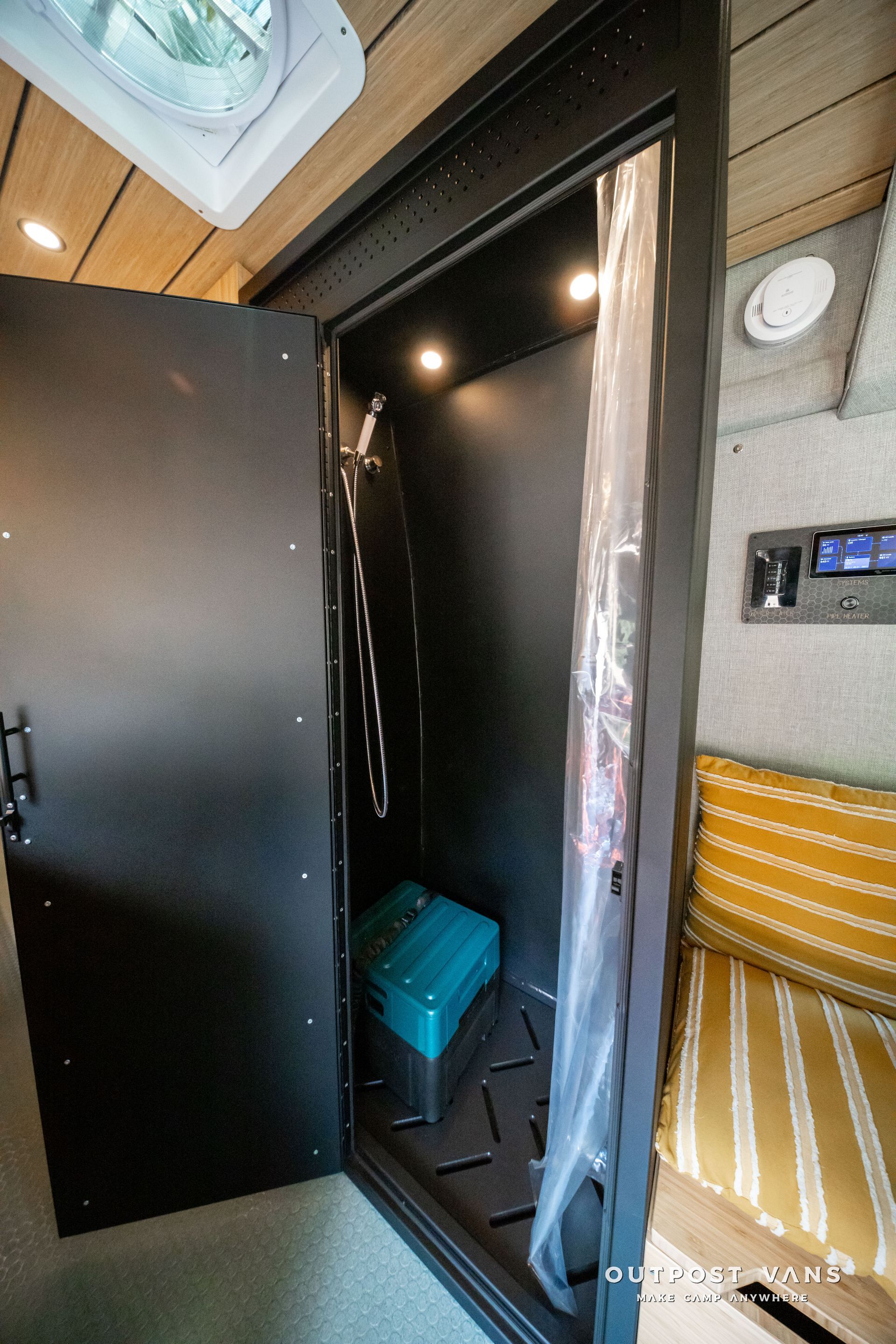 Small dark closet or shower stall with a blue bucket, wooden walls, and a striped cushion nearby