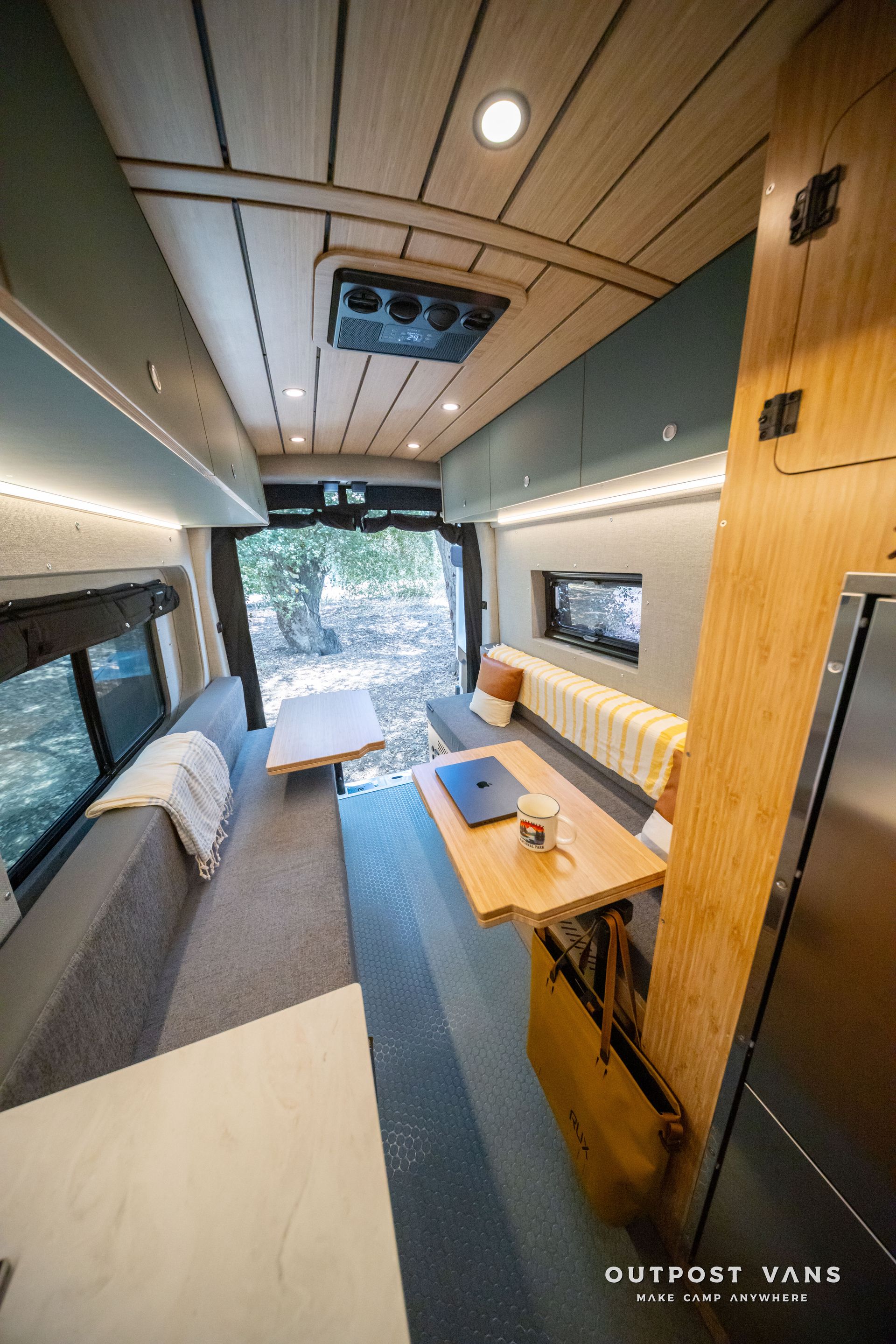 Modern camper van interior with bench seating, wood accents, skylight, and a small table by the window.