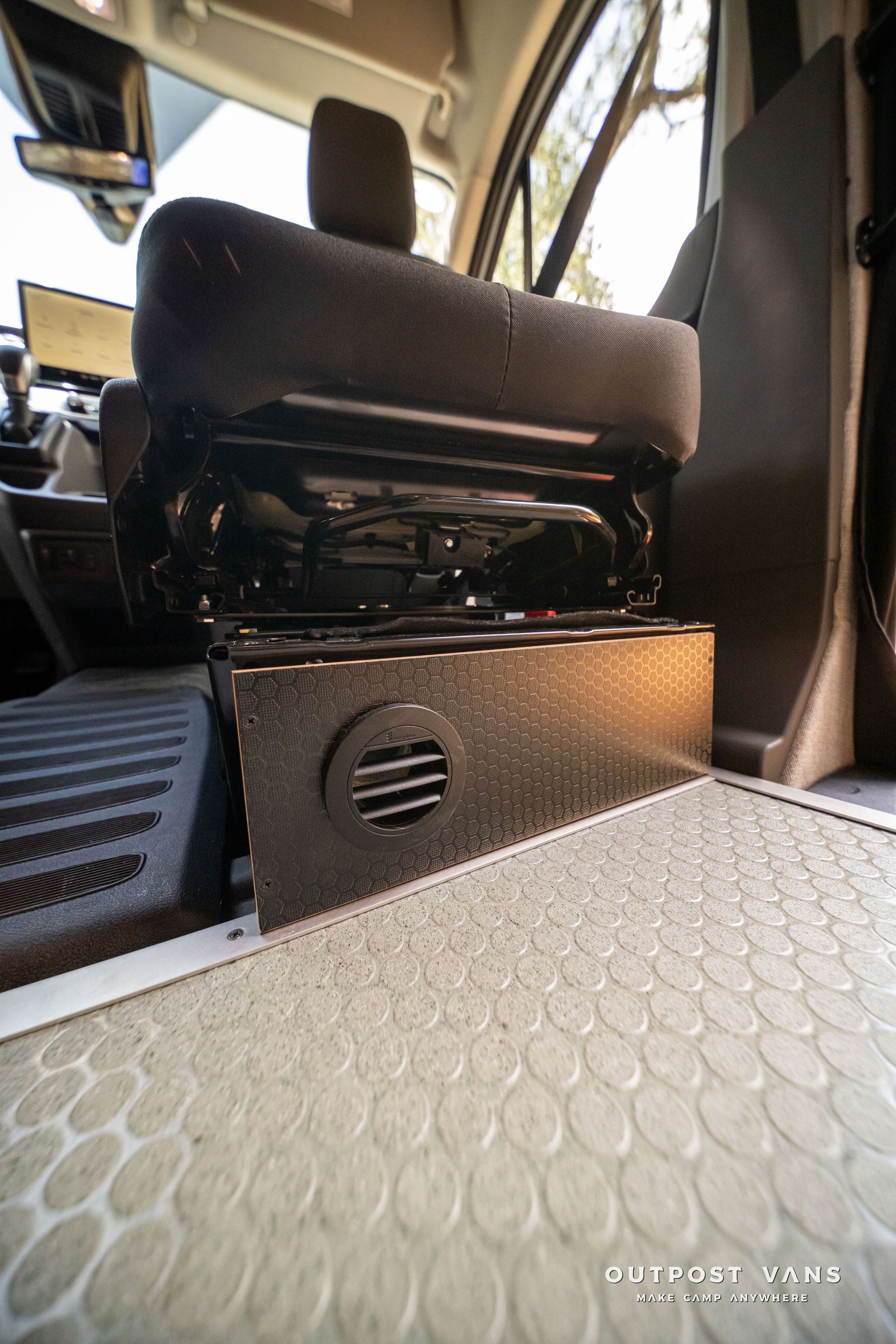 Bus interior with a black seat base and patterned floor mat near the aisle.