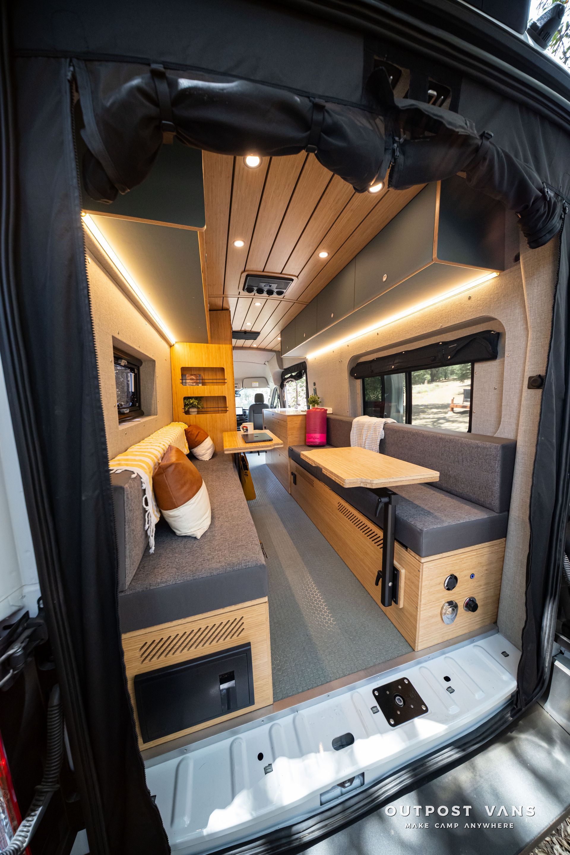 Compact van interior with bed, desk, and wood ceiling, viewed from the open rear door