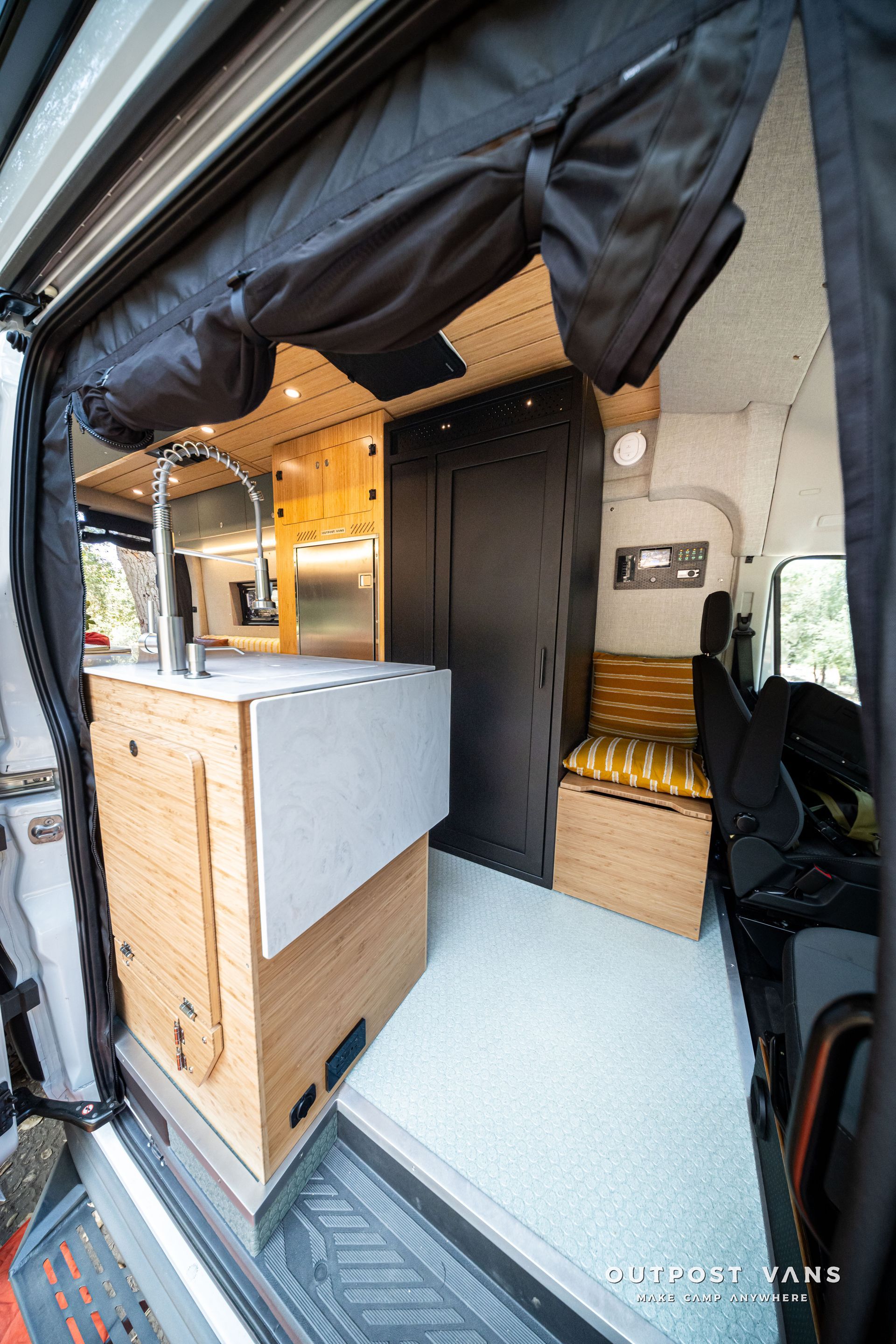 Compact camper van interior with wooden cabinets, bench seat, and open sliding door