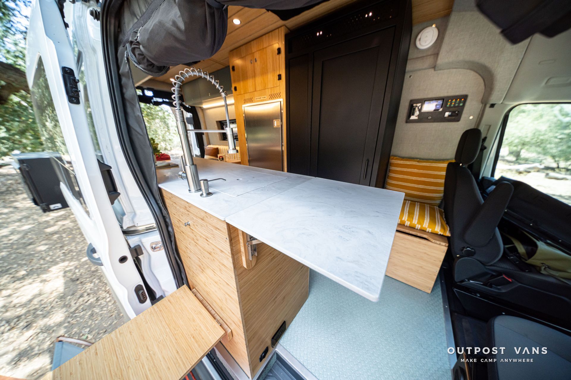 Compact camper interior with a fold-out table, wood cabinets, black curtains, and a bench seat