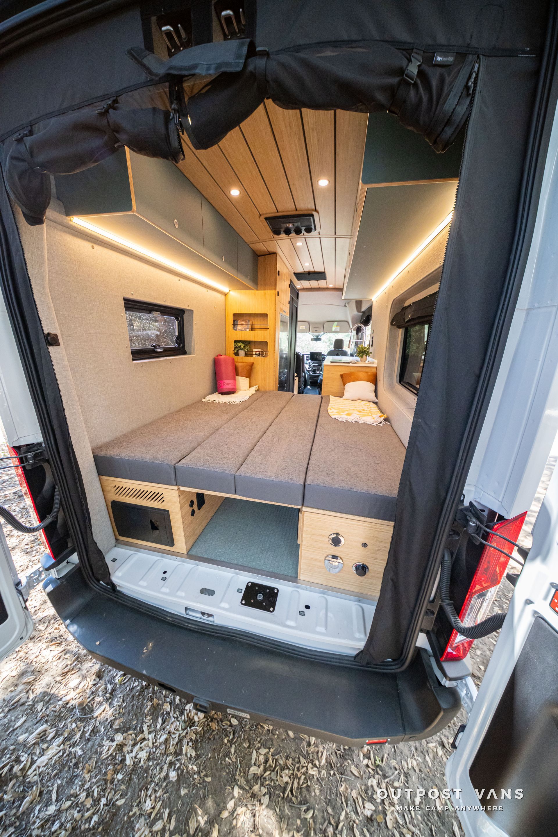 Van interior with a fold-out bed, wood ceiling, warm lighting, and storage cabinets