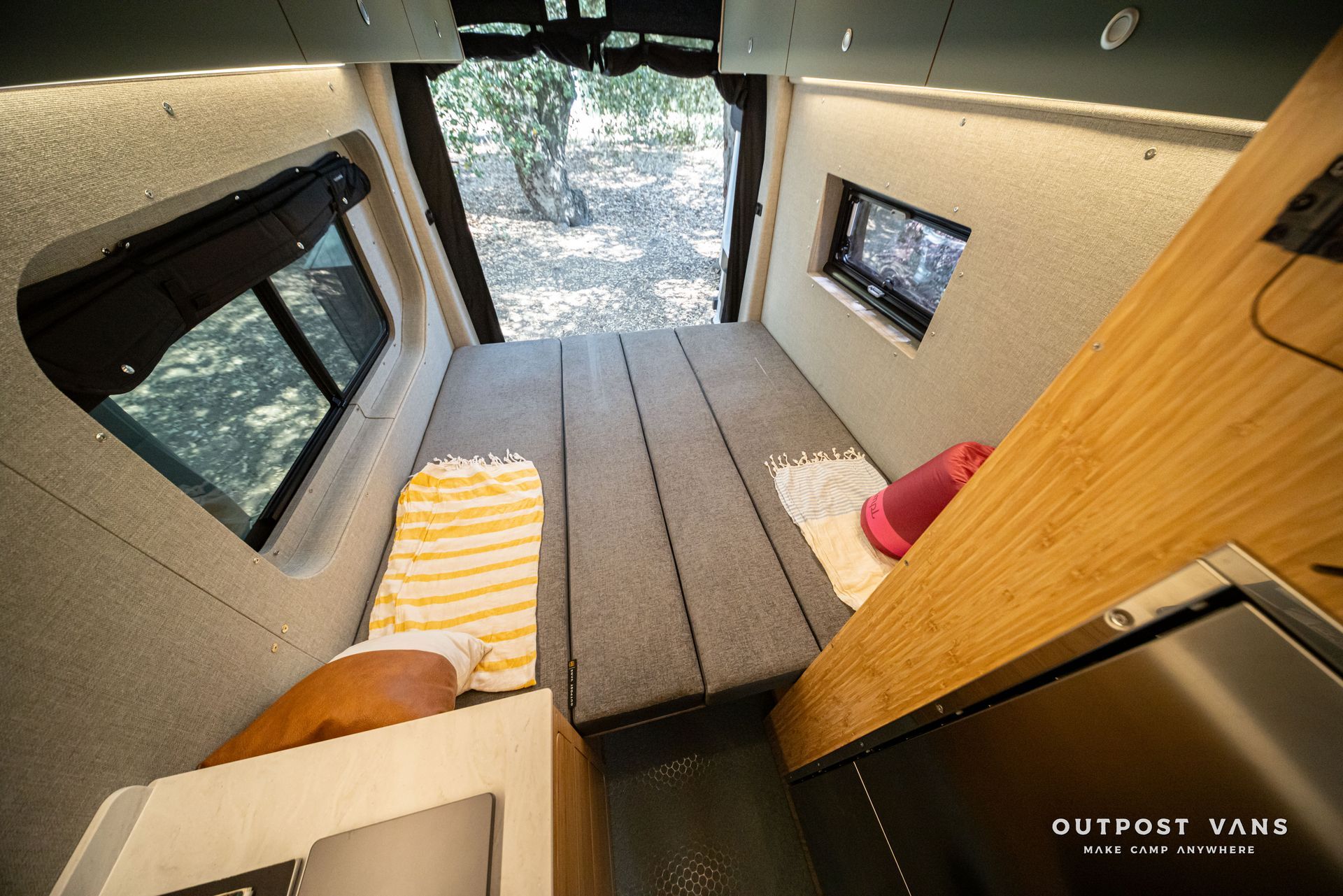 Compact van interior with a bed platform, gray floor, wood paneling, and side windows.
