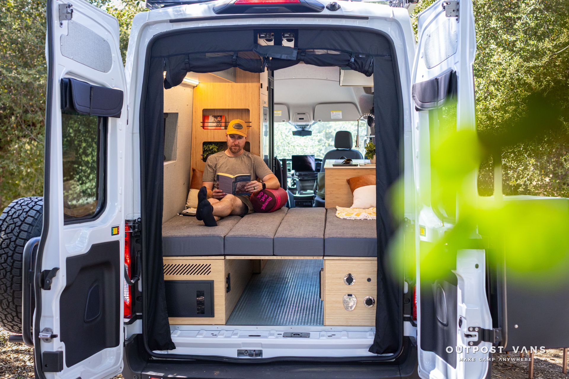 Person relaxing inside a van camper with open rear doors and warm interior lighting