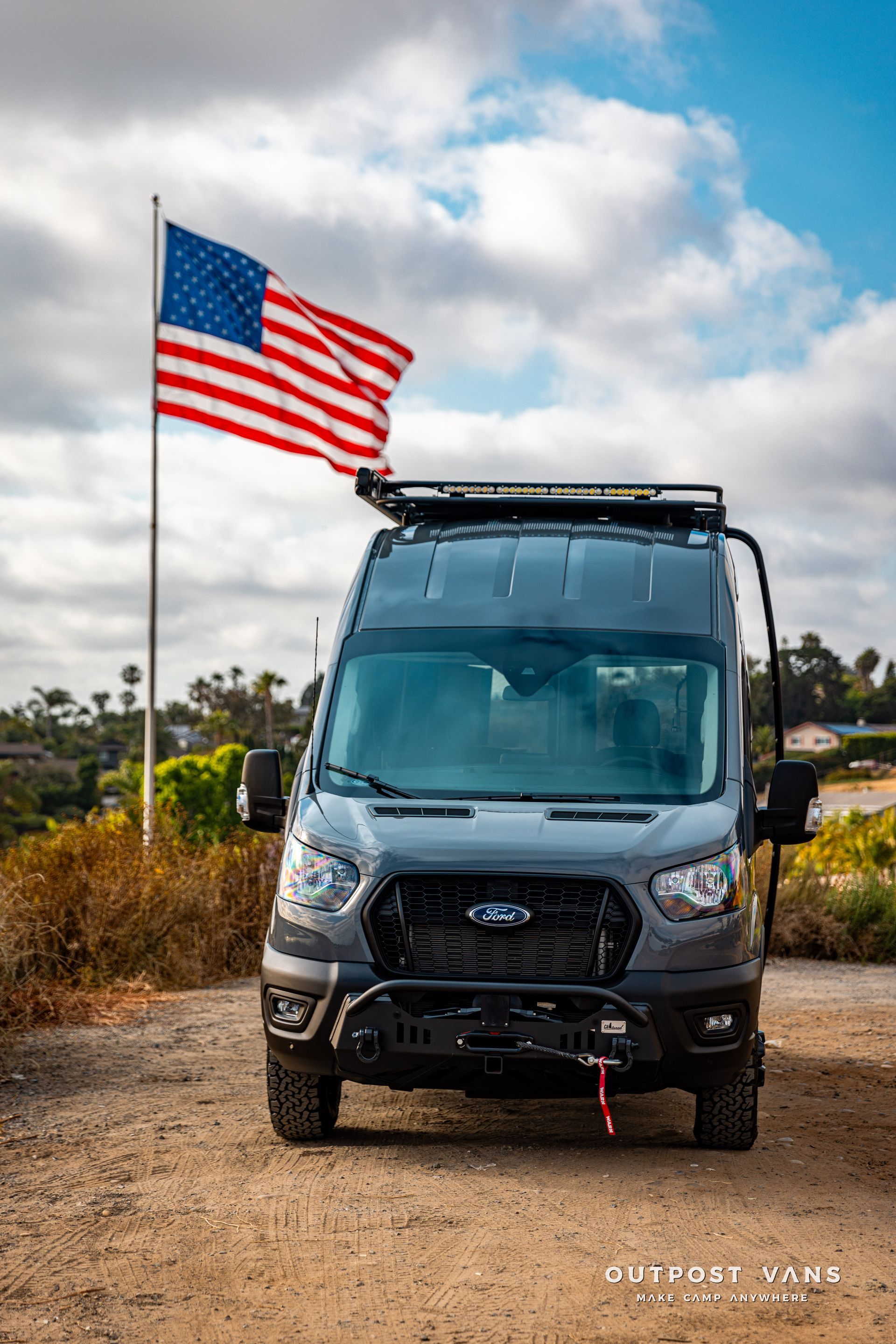 a van with an american flag on top of it is parked on a dirt road .