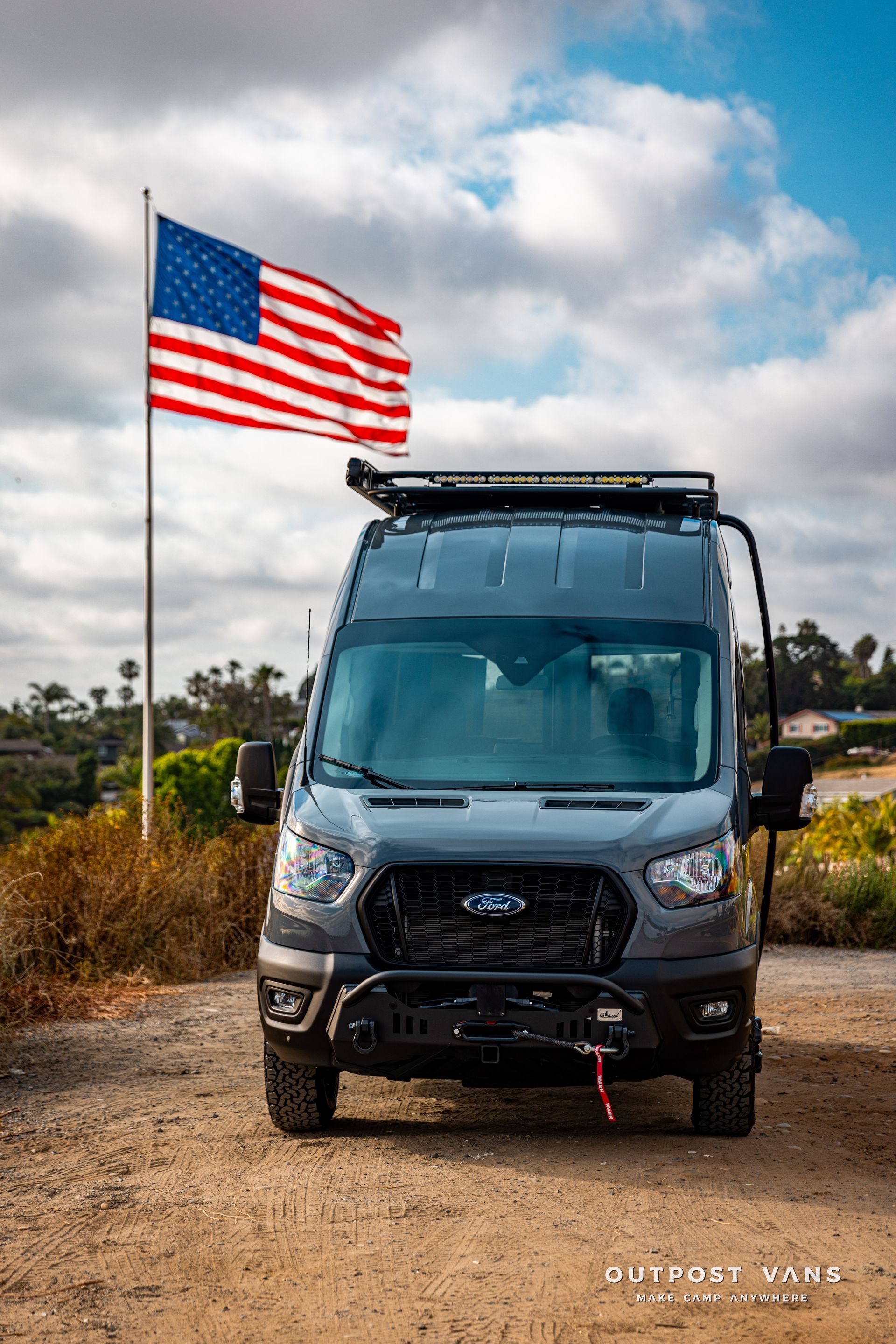 a van with an american flag on top of it is parked on the side of a dirt road .