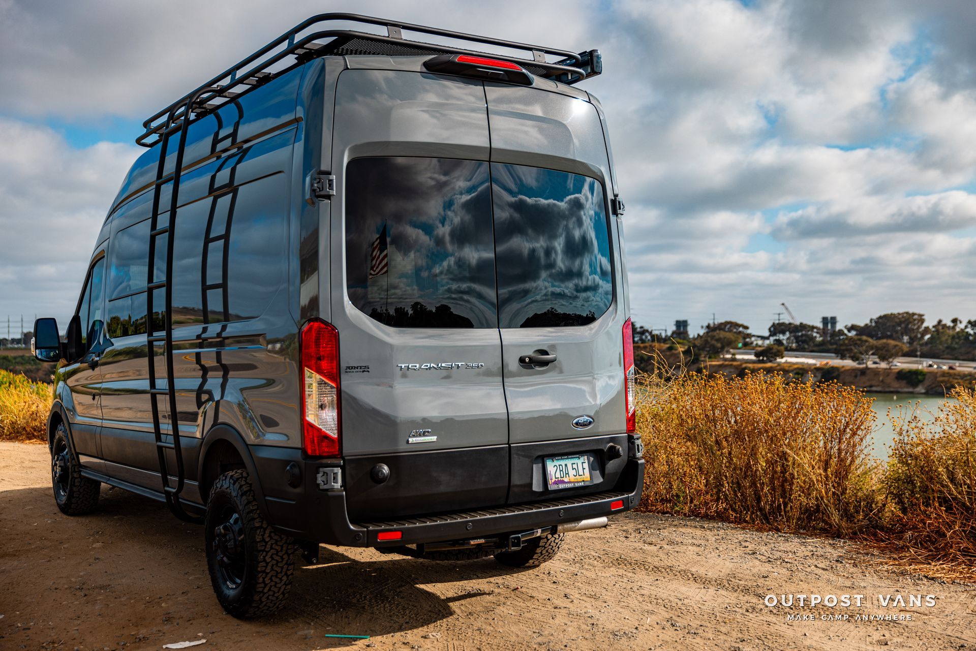 a gray van with a ladder on the roof is parked on a dirt road .