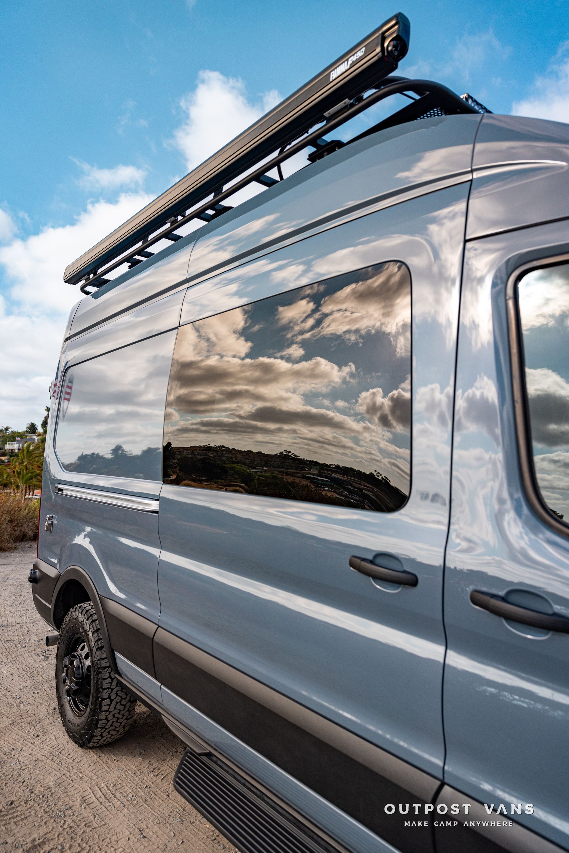 a gray van with a light on top of it is parked on a dirt road .