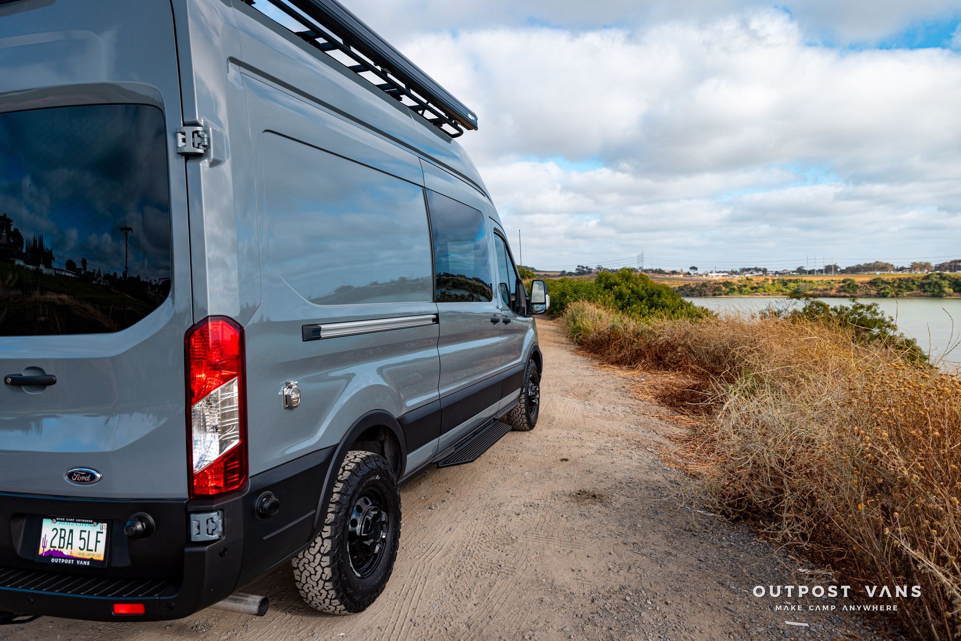 a gray van is parked on a dirt road next to a body of water .