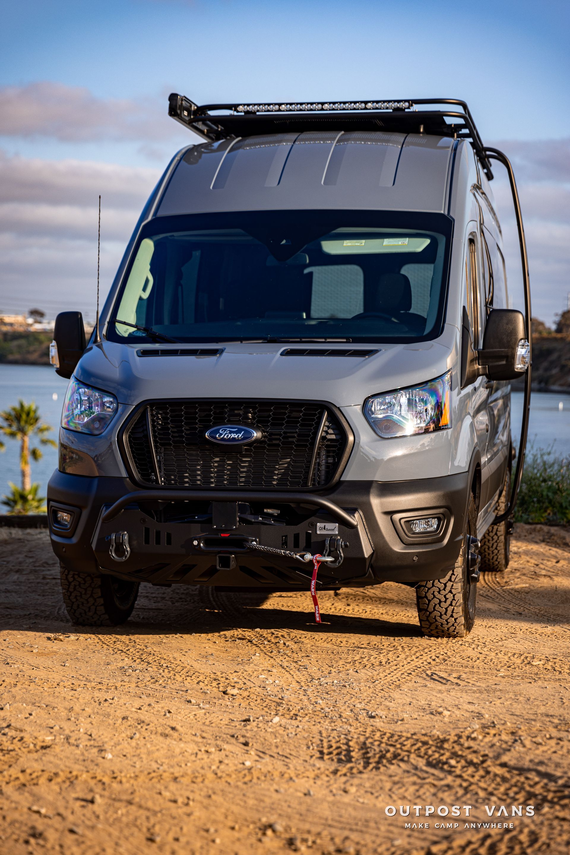 a ford transit van is parked on a dirt road next to a body of water .
