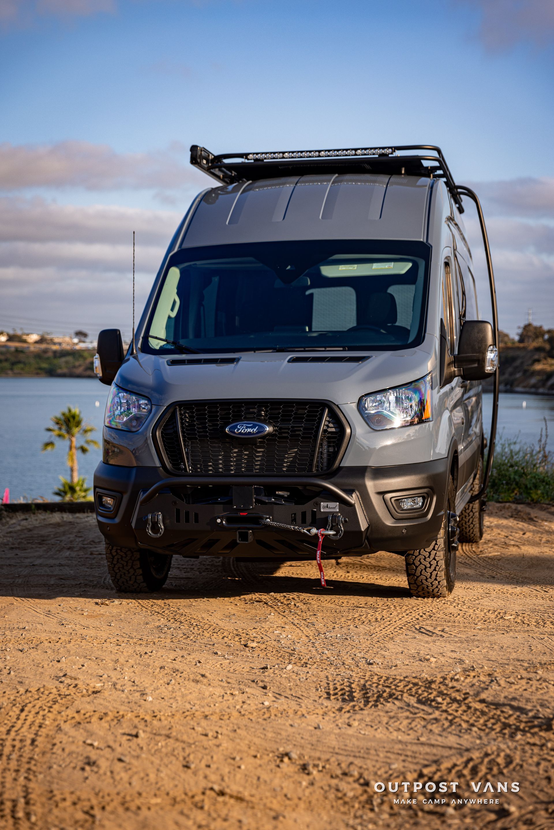 a ford transit van is parked on a dirt road next to a body of water .
