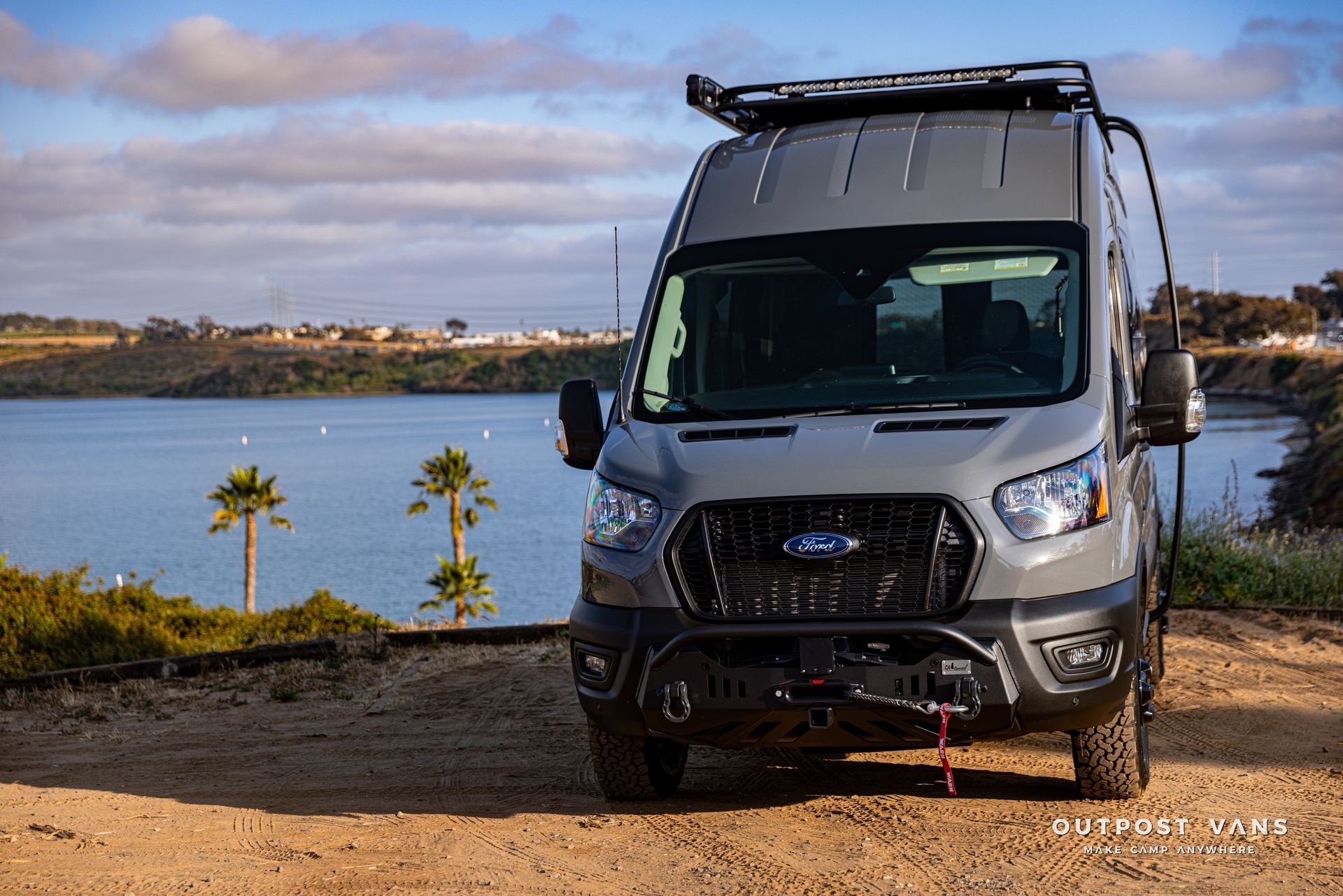 a van is parked on a dirt road next to a body of water .