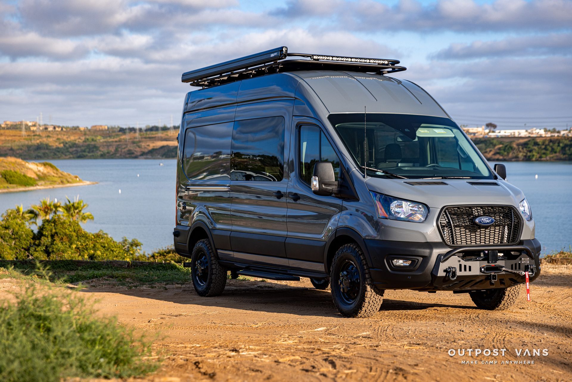 A van is parked on top of a dirt hill next to a body of water.