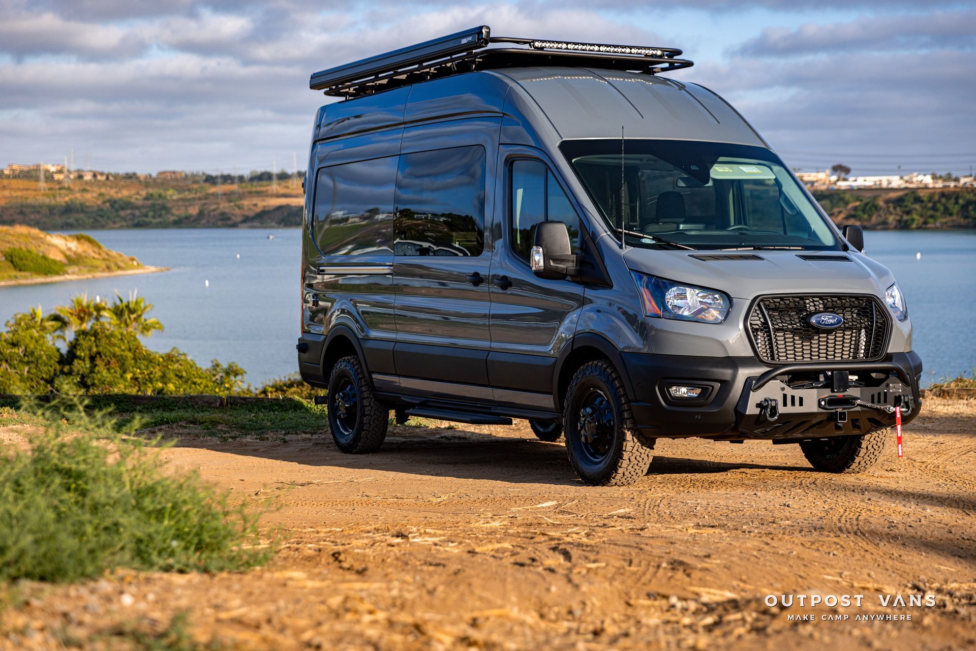 a van is parked on top of a dirt hill next to a body of water .
