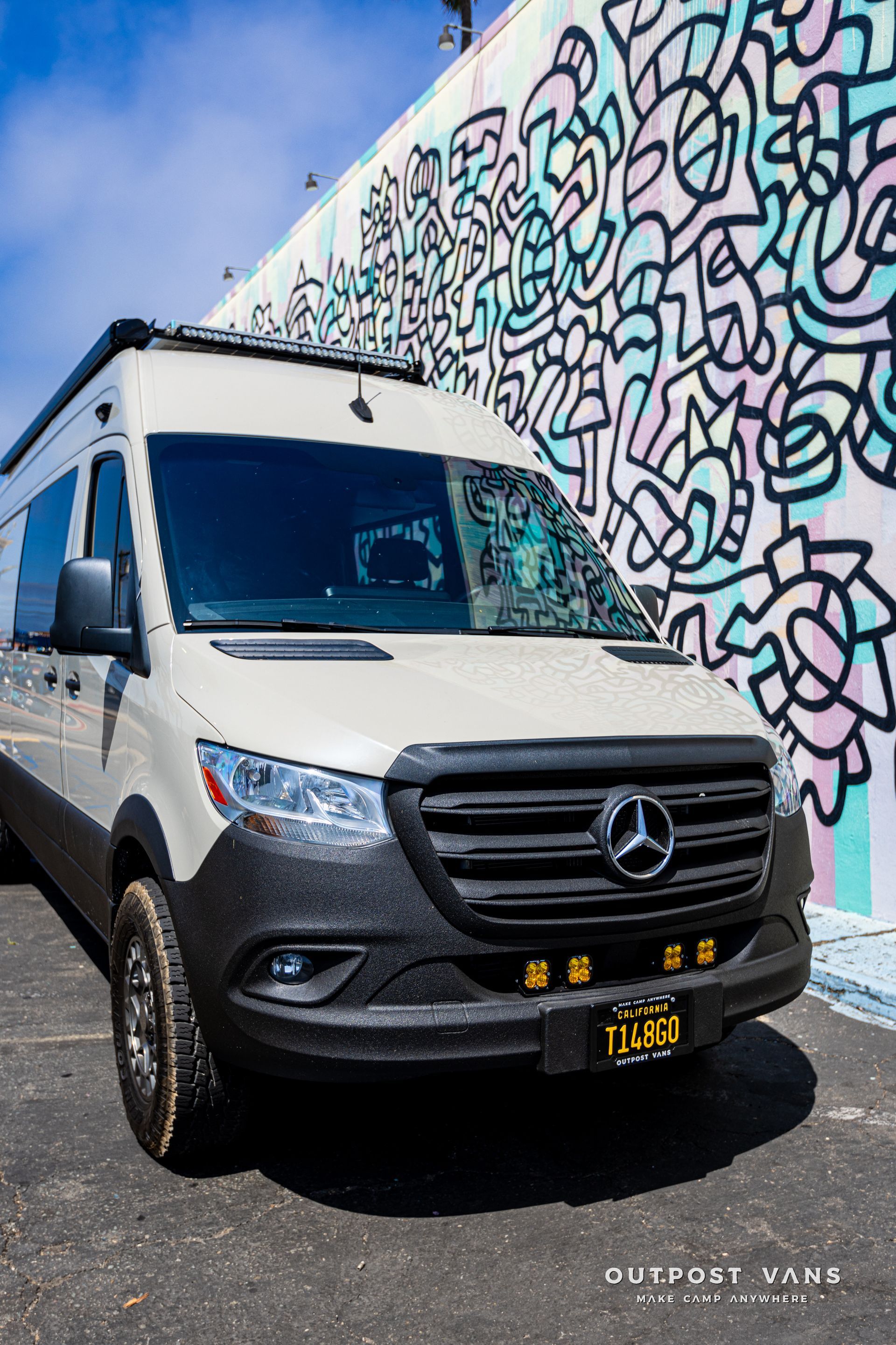 A white mercedes van is parked in front of a graffiti covered wall.
