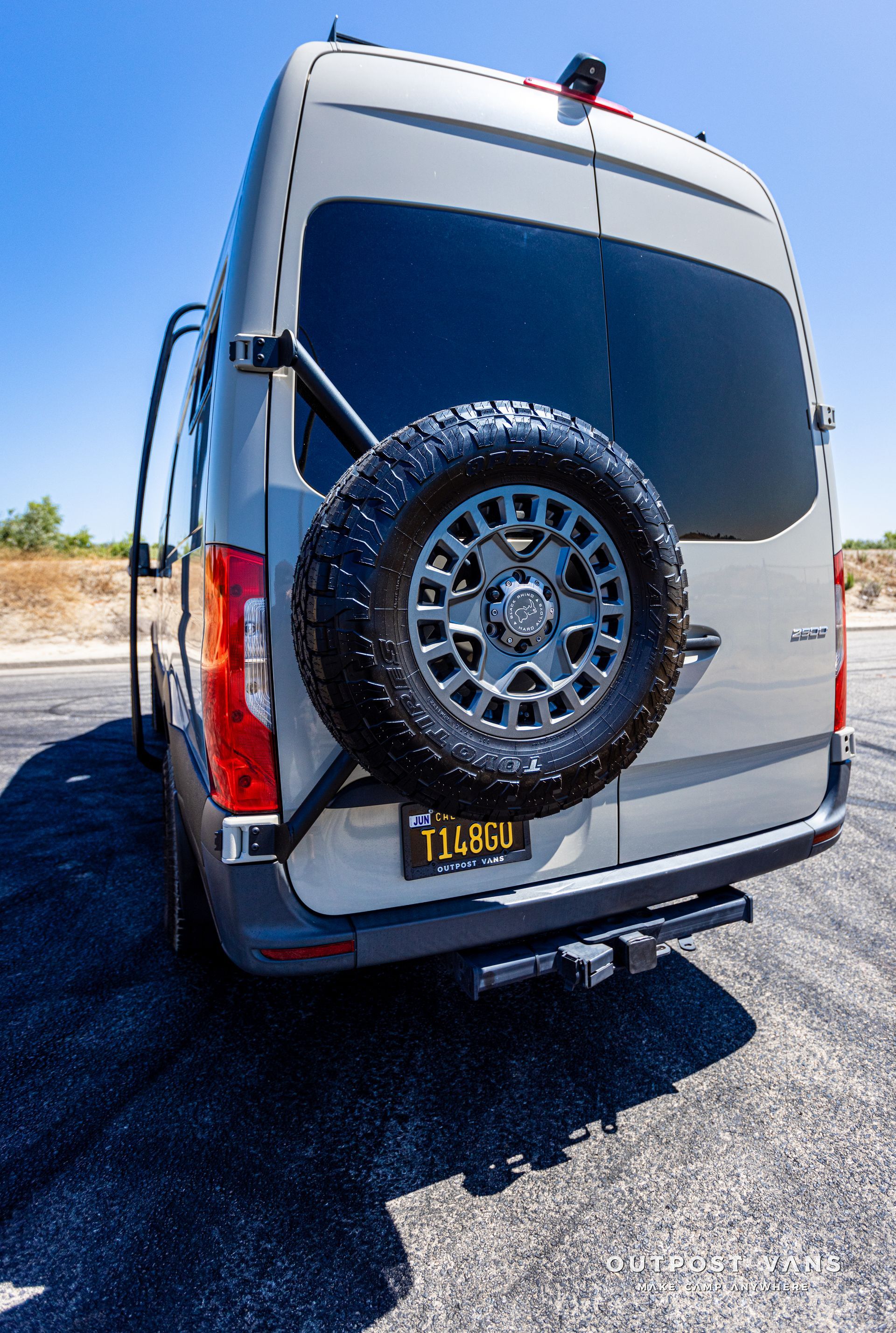 A white van with a spare tire attached to the back is parked on the side of the road.