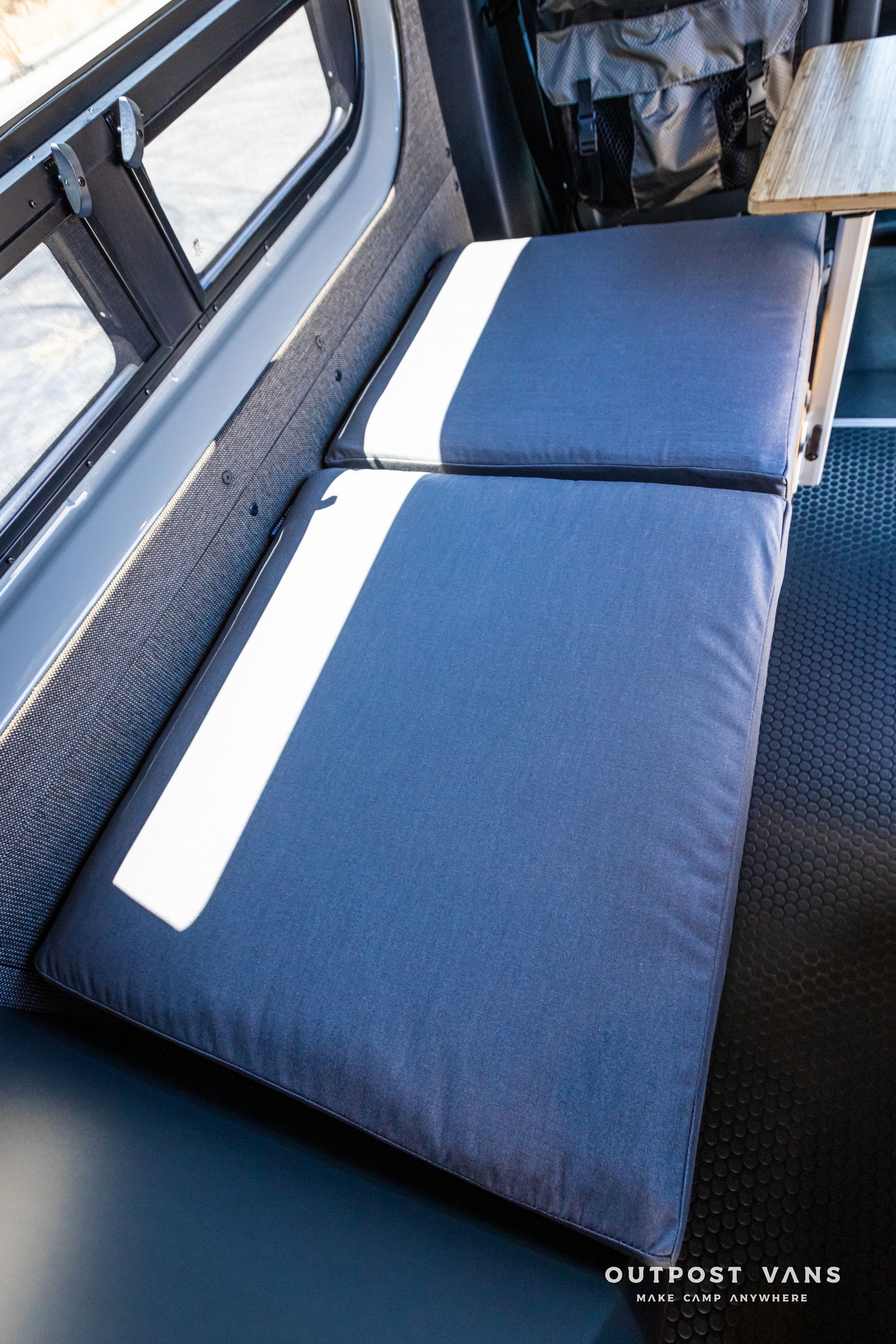 A couch in a van with blue cushions and a wooden table.