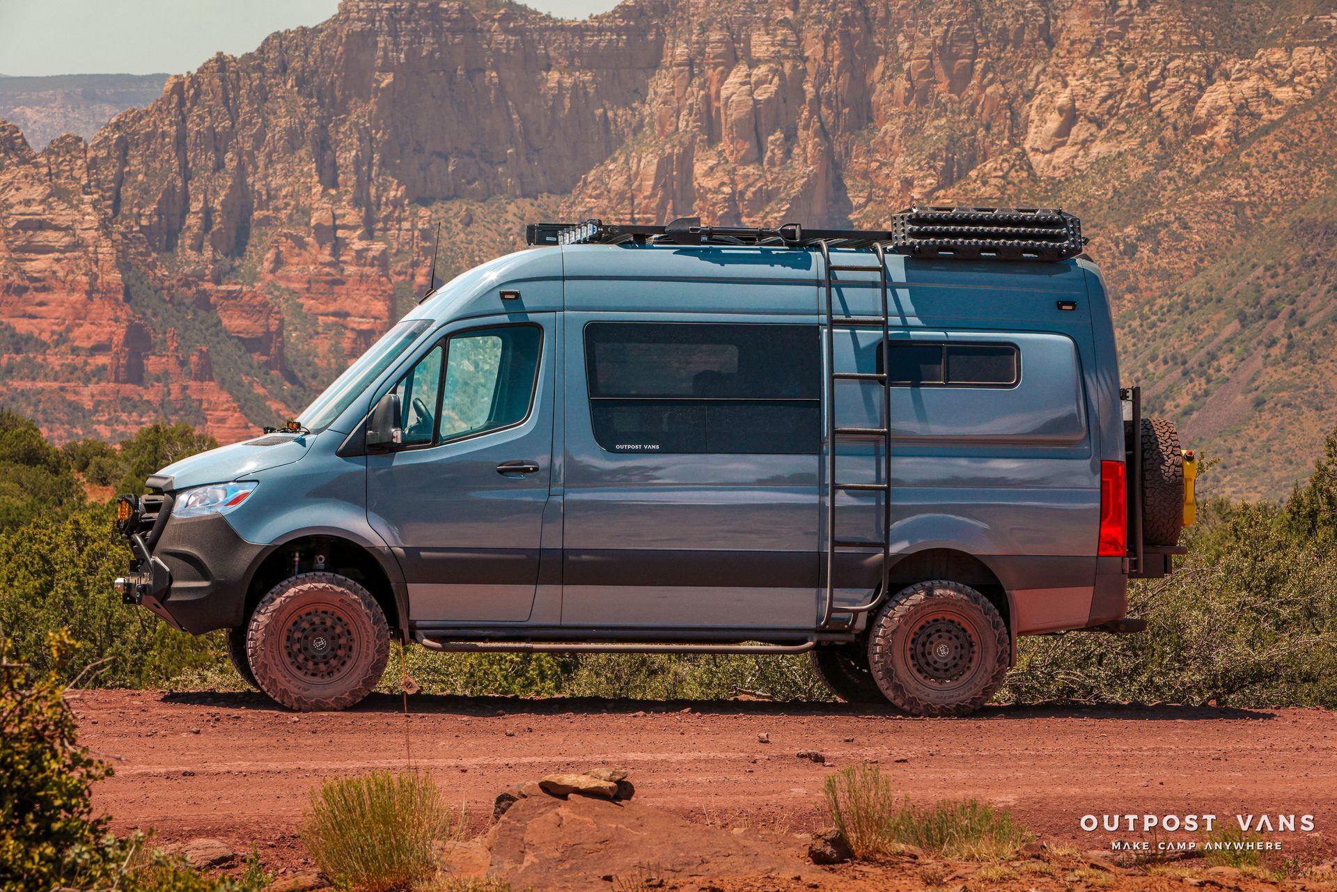 a blue van is parked on the side of a dirt road in front of a mountain .