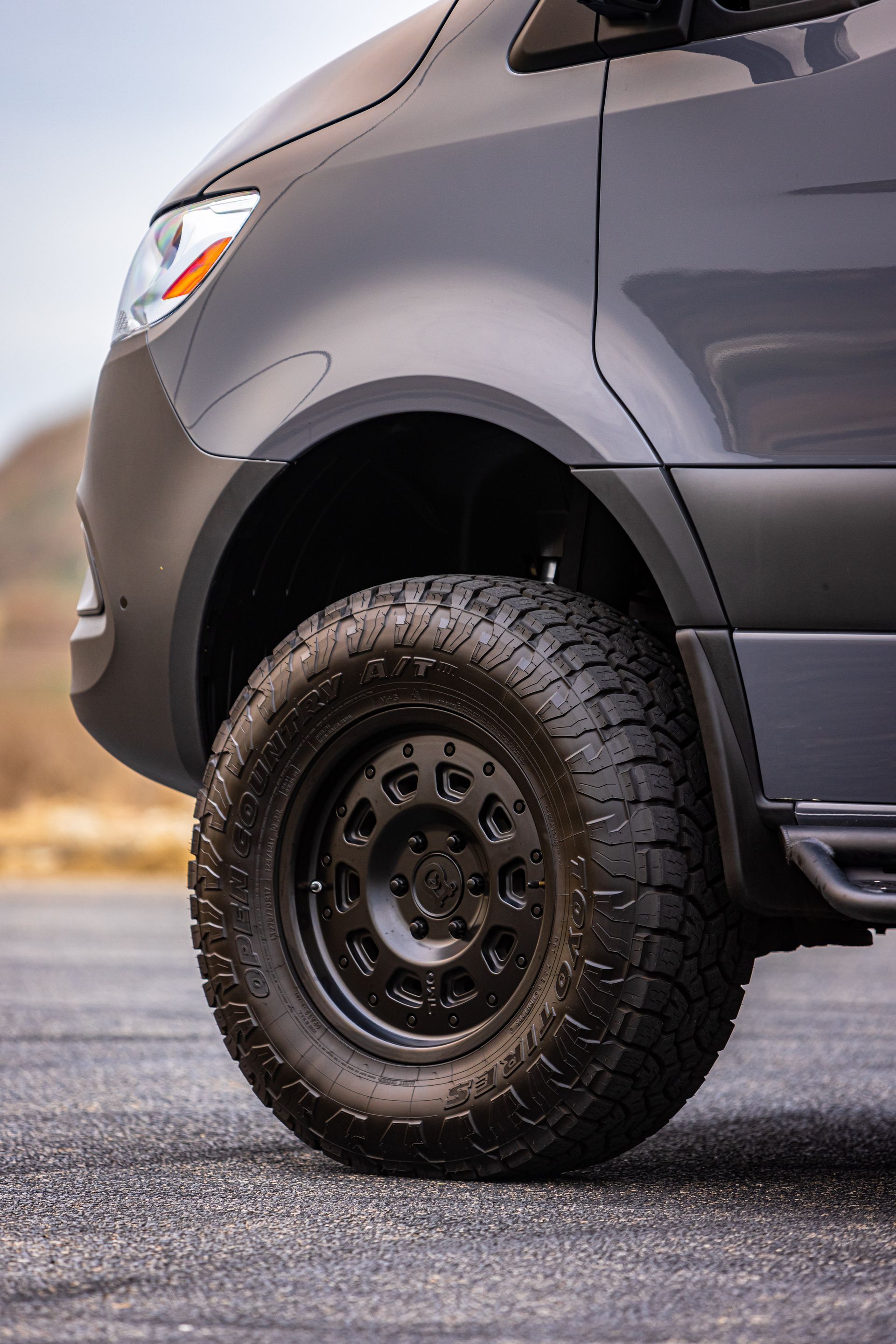 A black van with a black tire is parked on the side of the road.