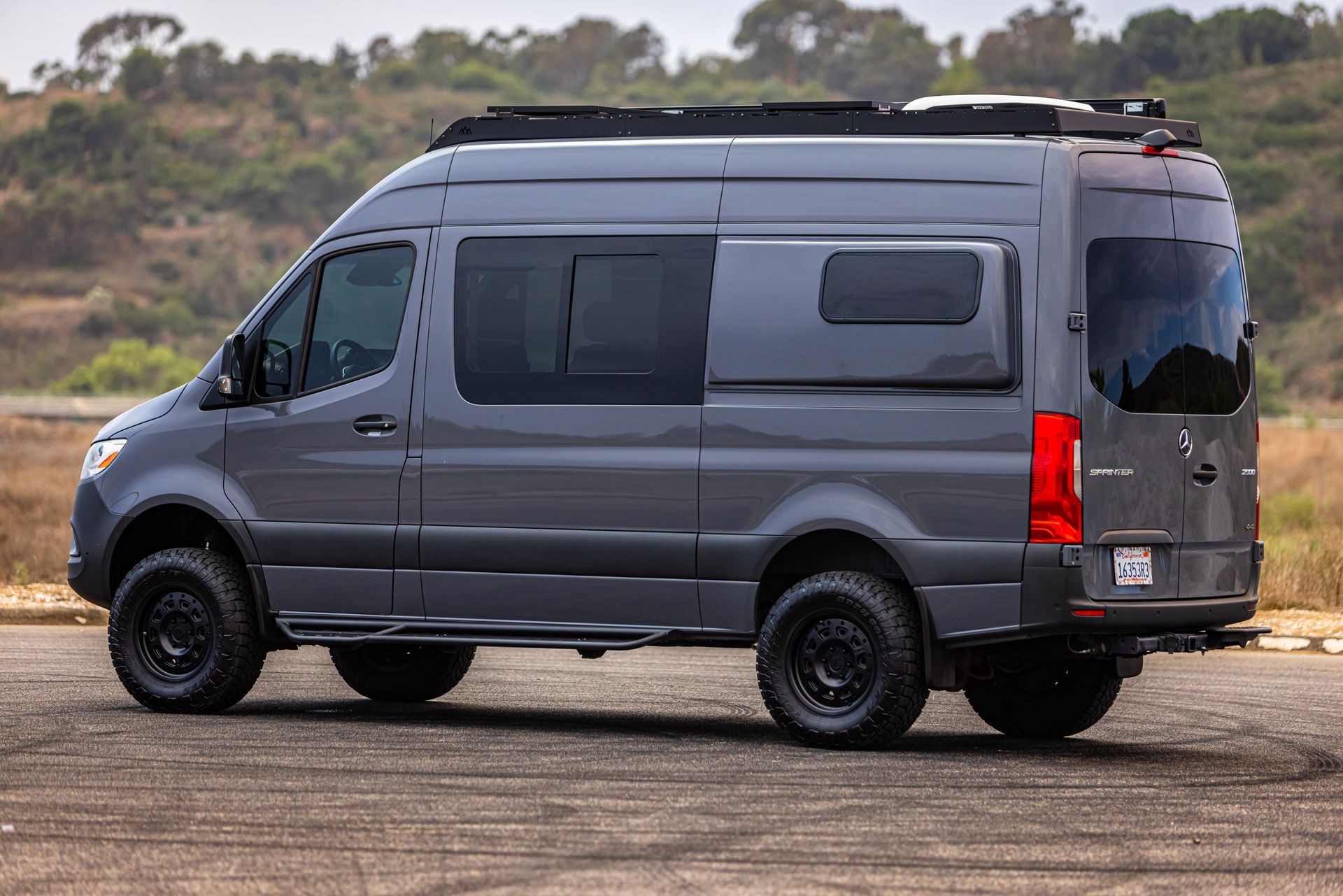 A gray van is parked on a dirt road.