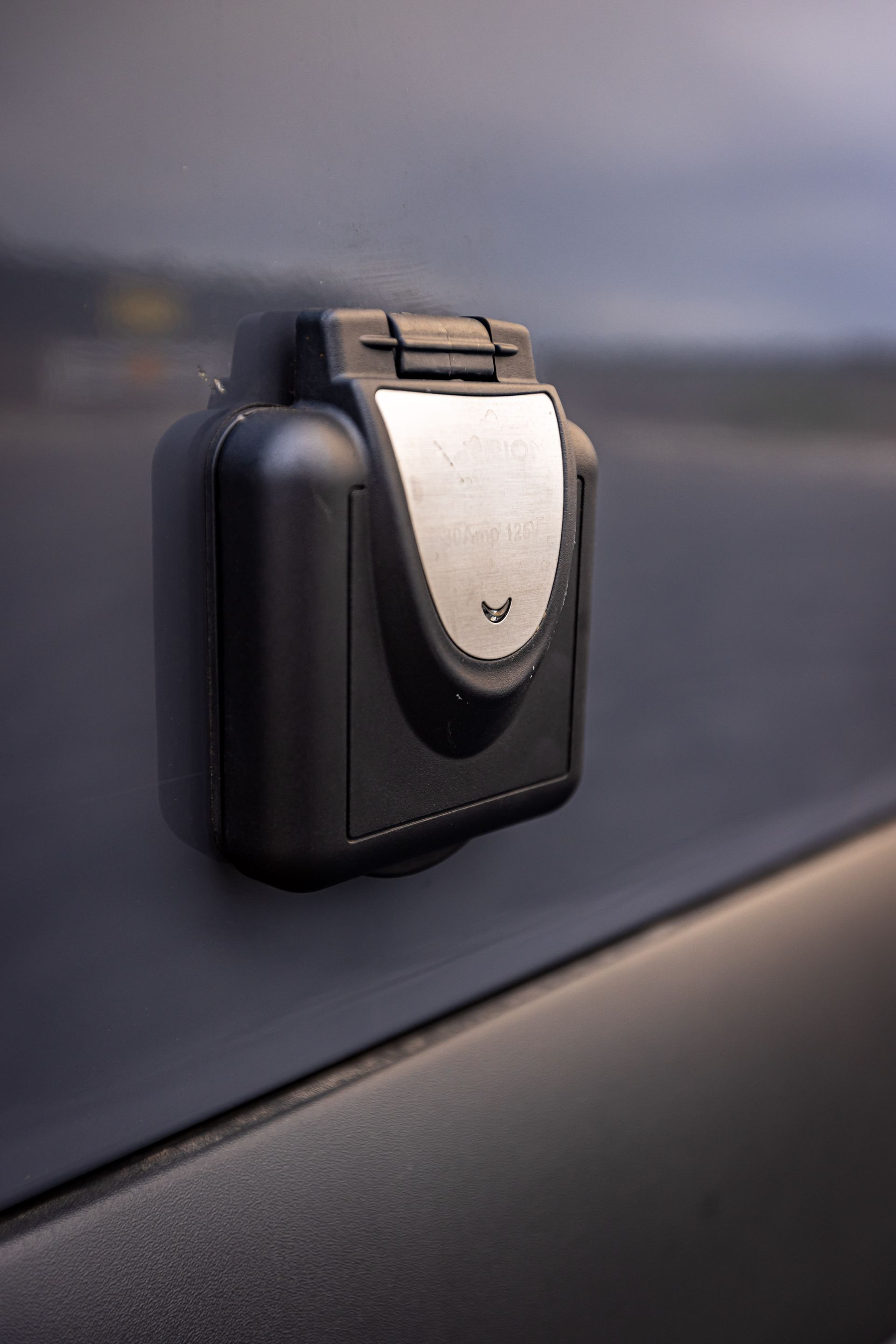 A close up of a black electrical outlet on the side of a car.