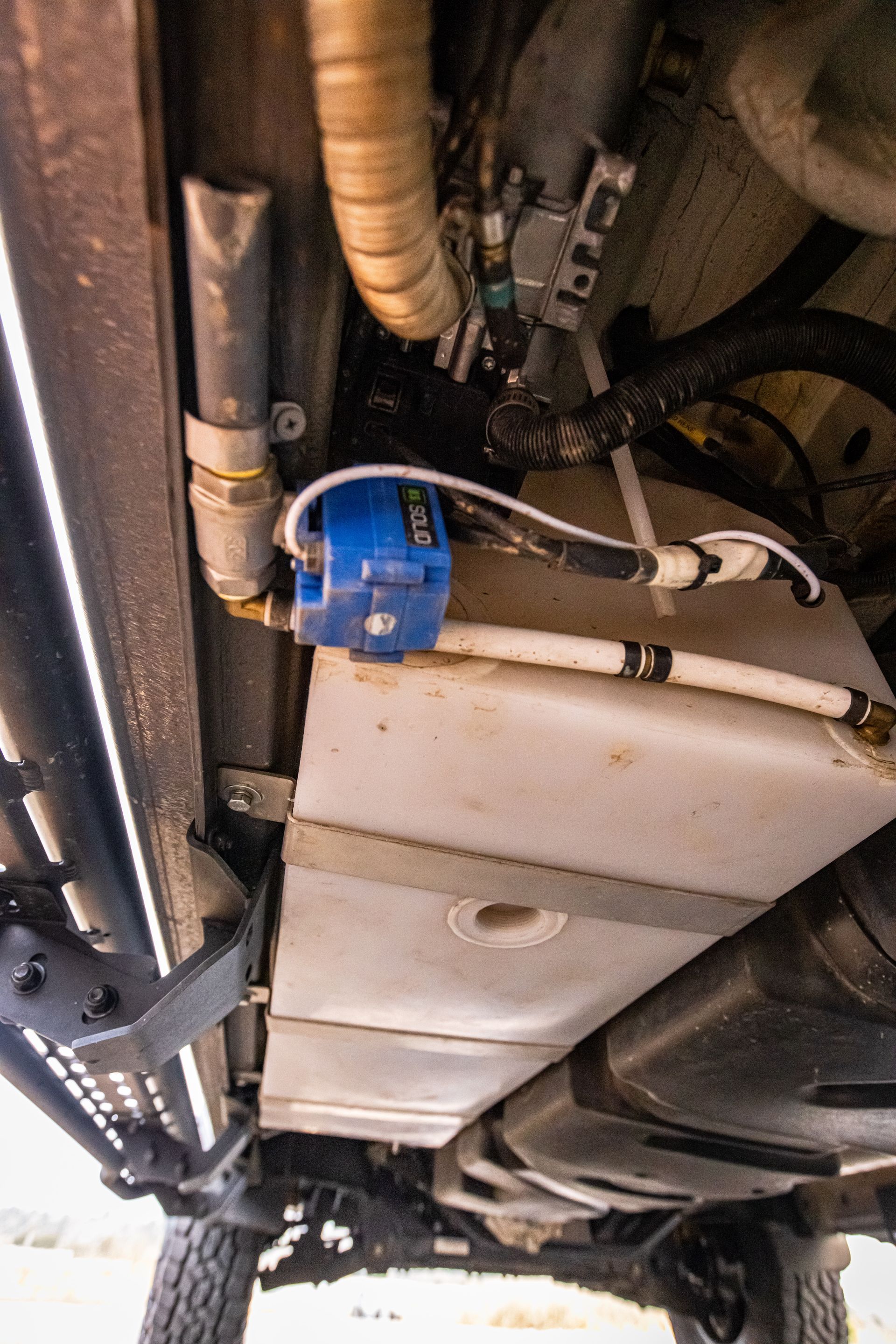 A water tank is attached to the underside of a vehicle.