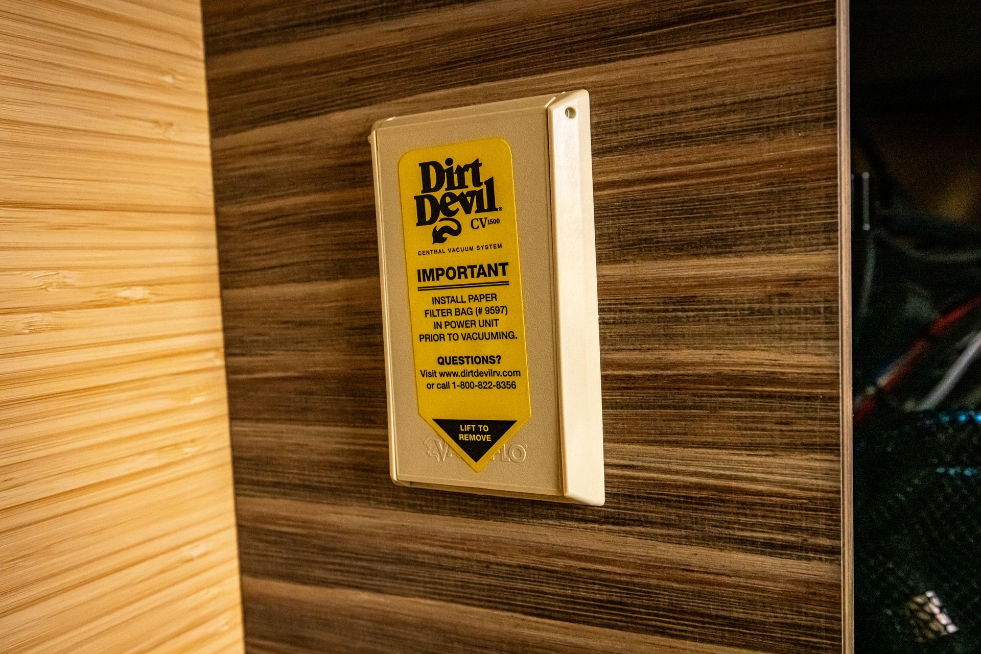 A white box with a yellow sticker on it is hanging on a wooden wall.