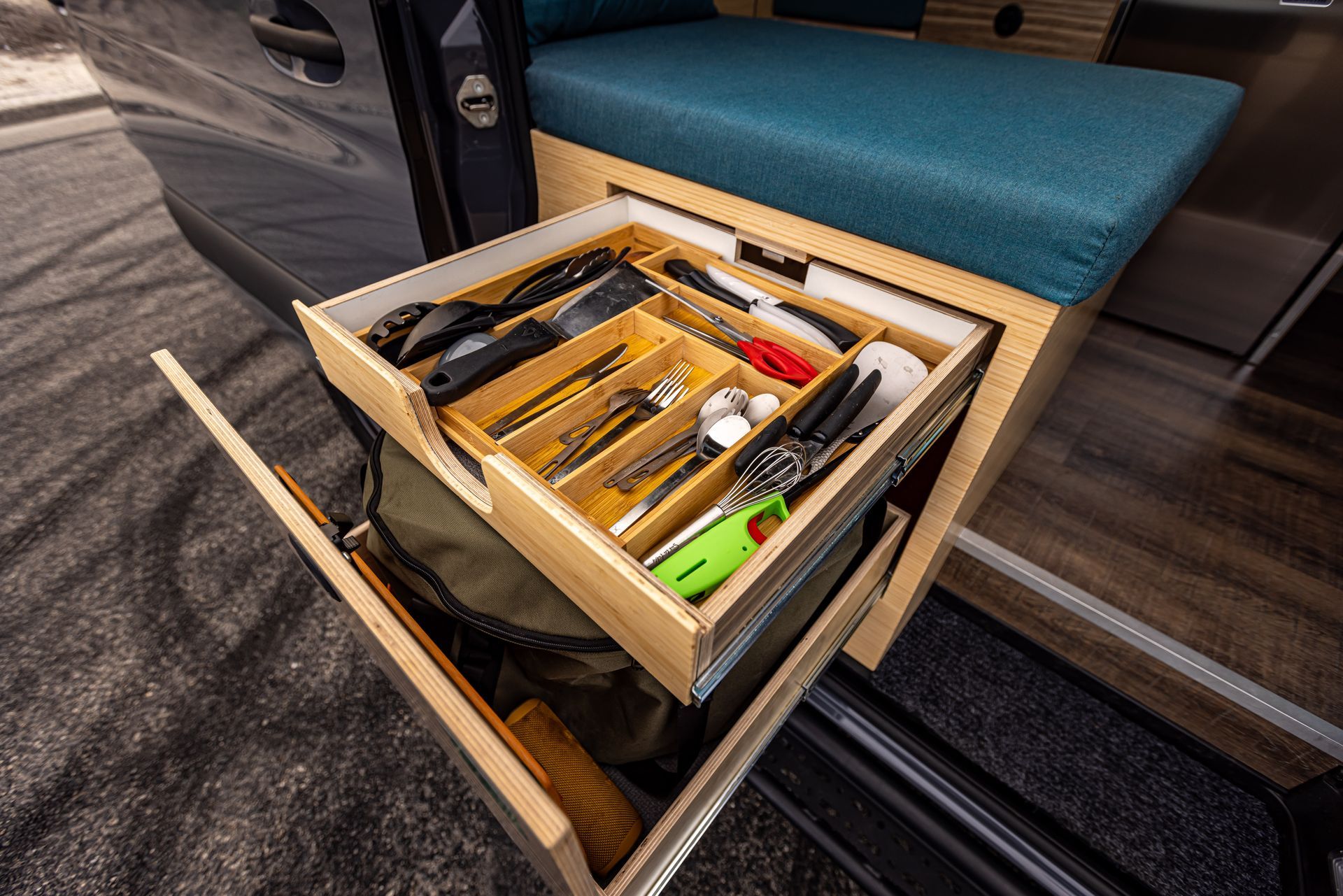 A drawer filled with utensils and a bag in a camper van.