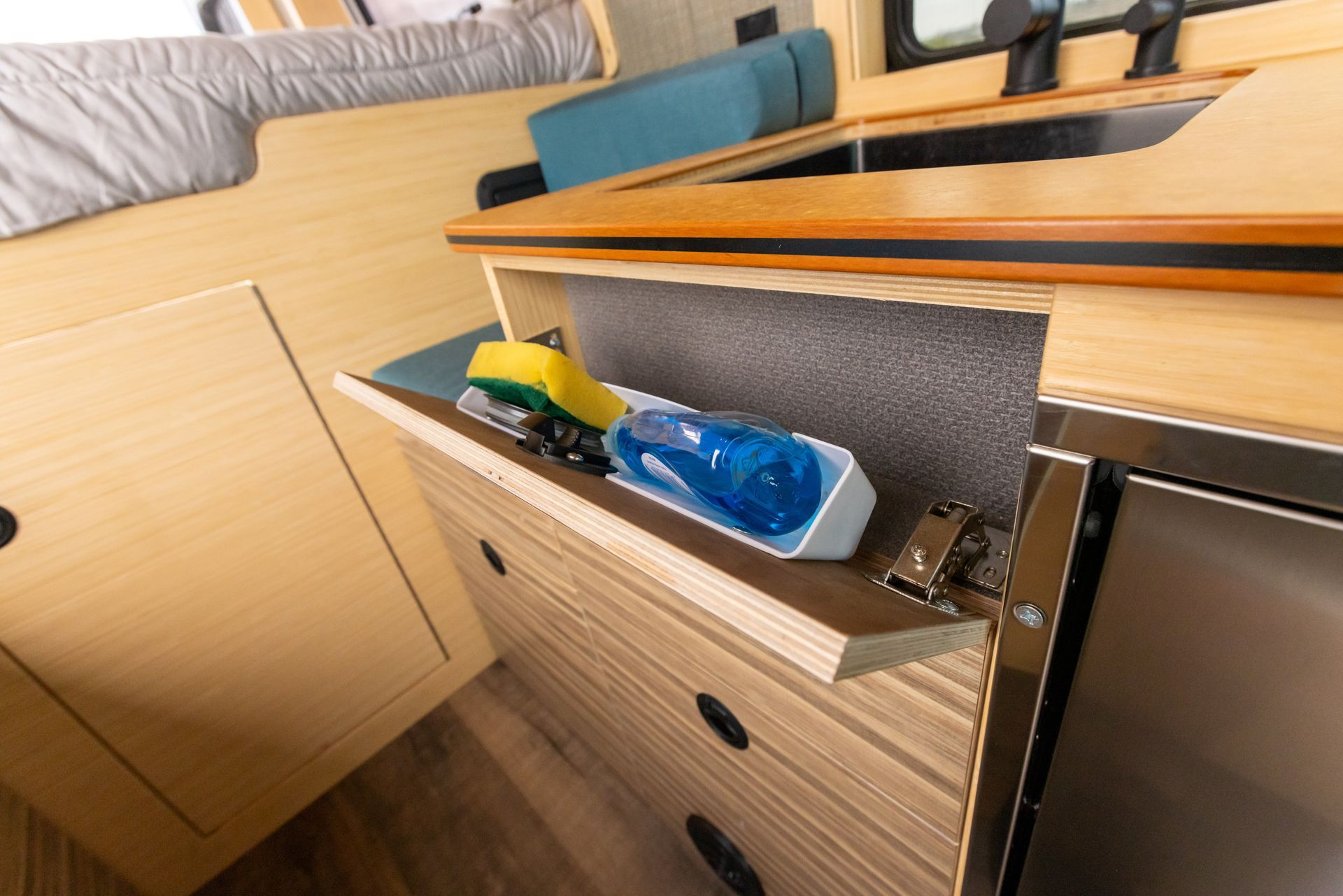 A sponge and a bottle are in a drawer in a kitchen.