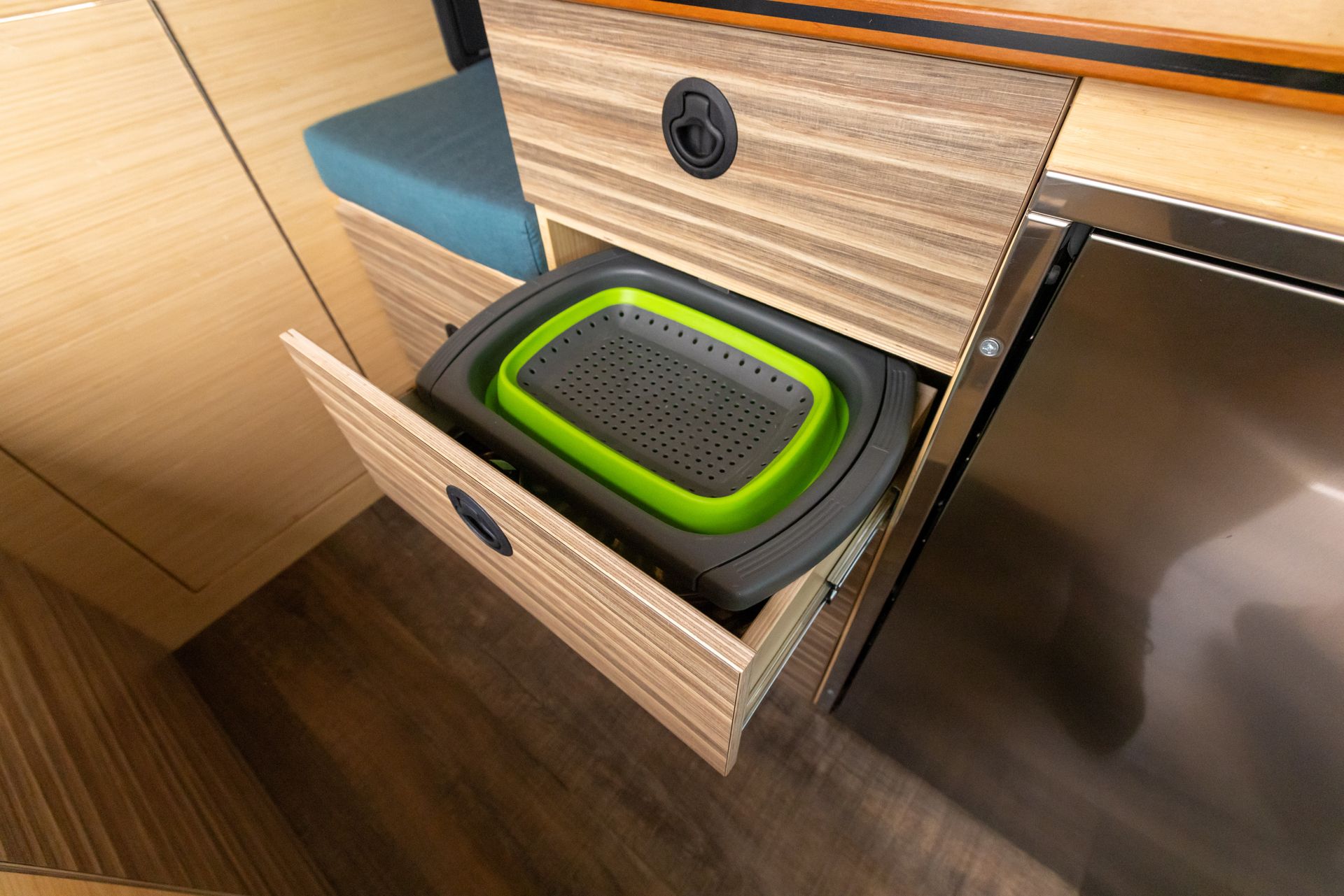 A kitchen drawer with a green strainer in it.