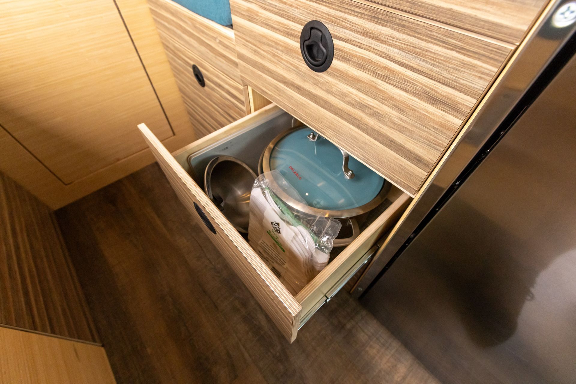 A wooden drawer filled with pots and pans in a kitchen.