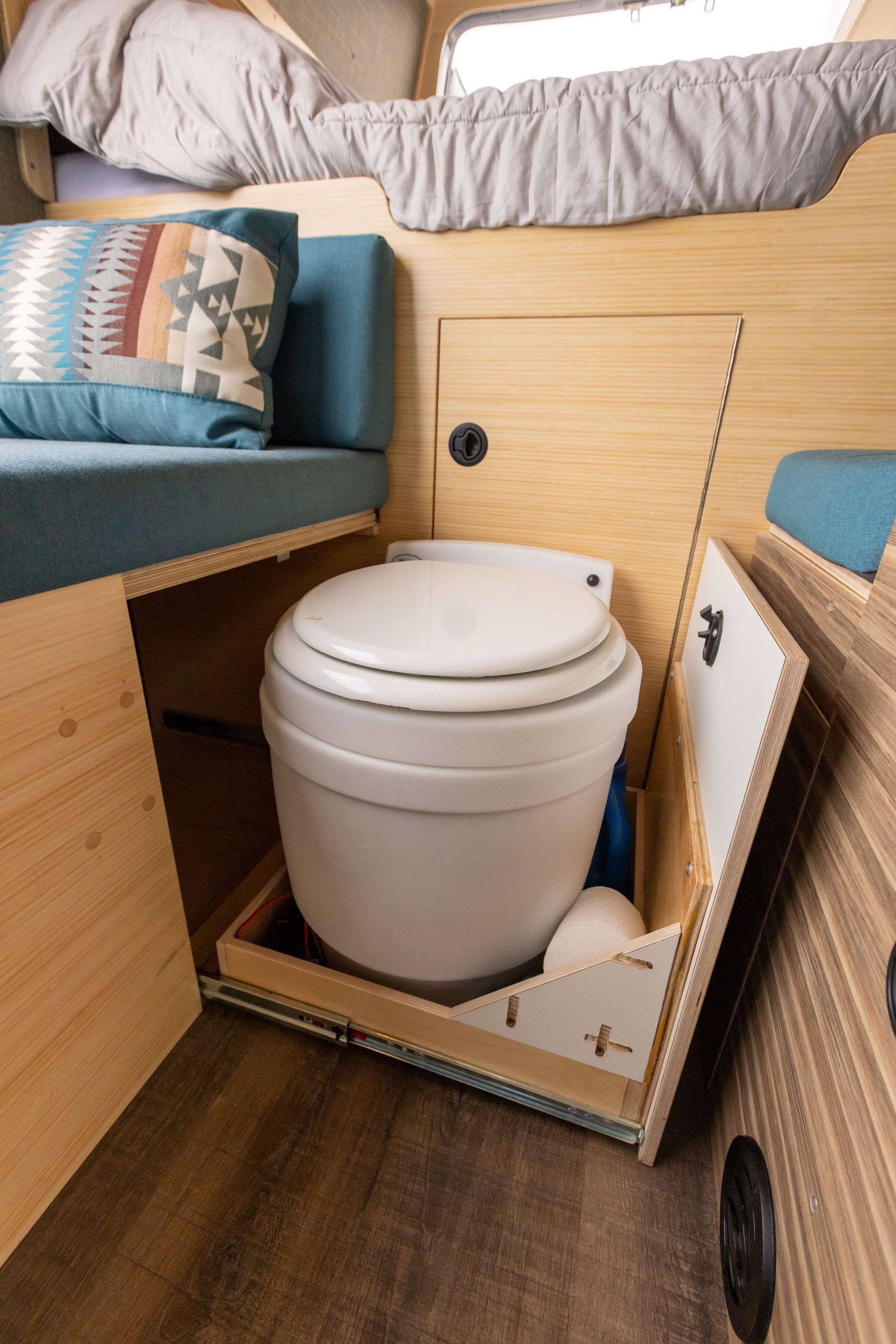 A toilet is sitting under a bed in a camper van.