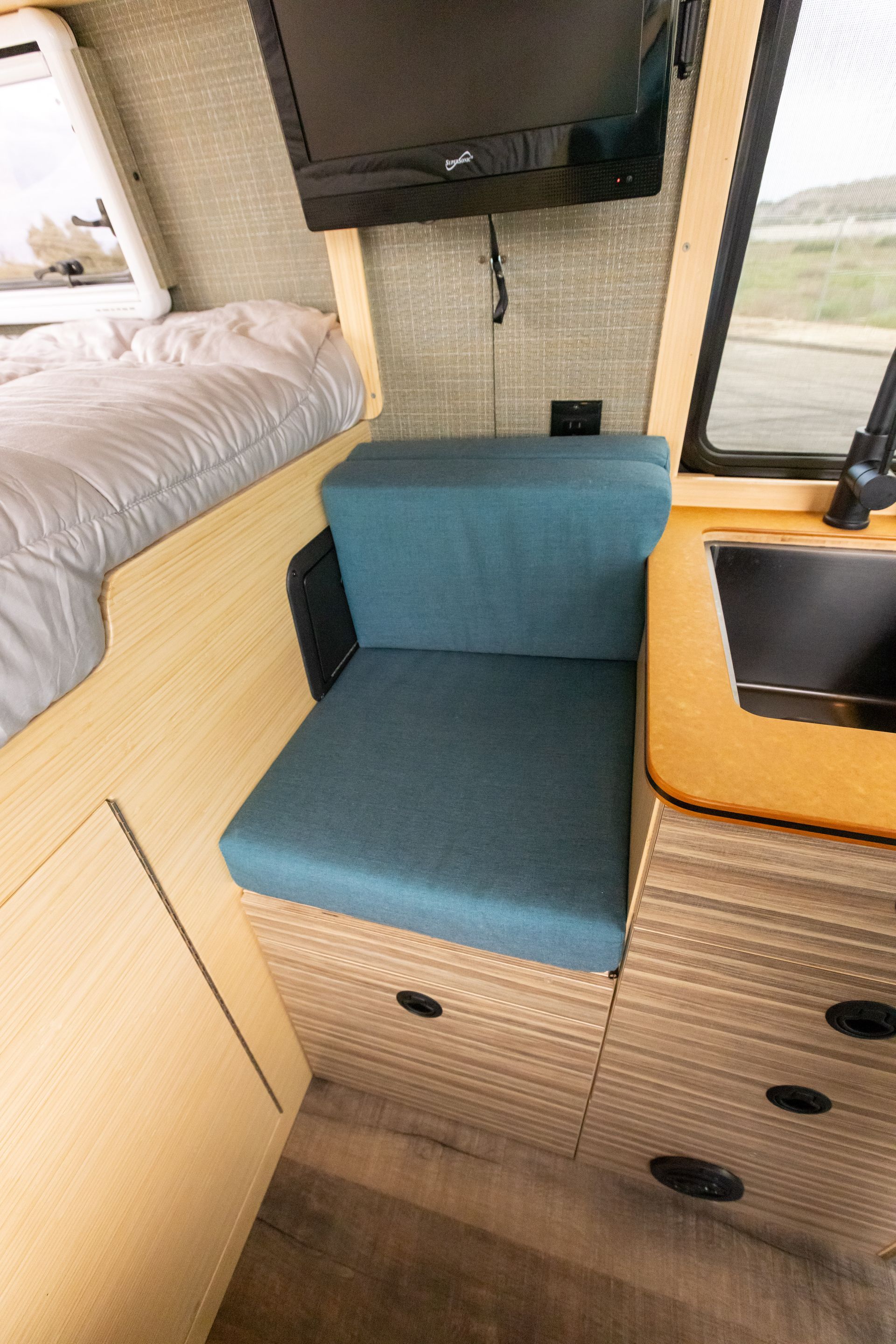A chair with a blue cushion is in a room with a television and a sink.
