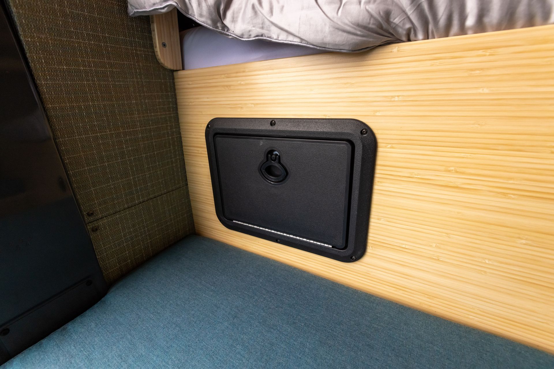 A small black box is sitting on a wooden wall next to a bed.
