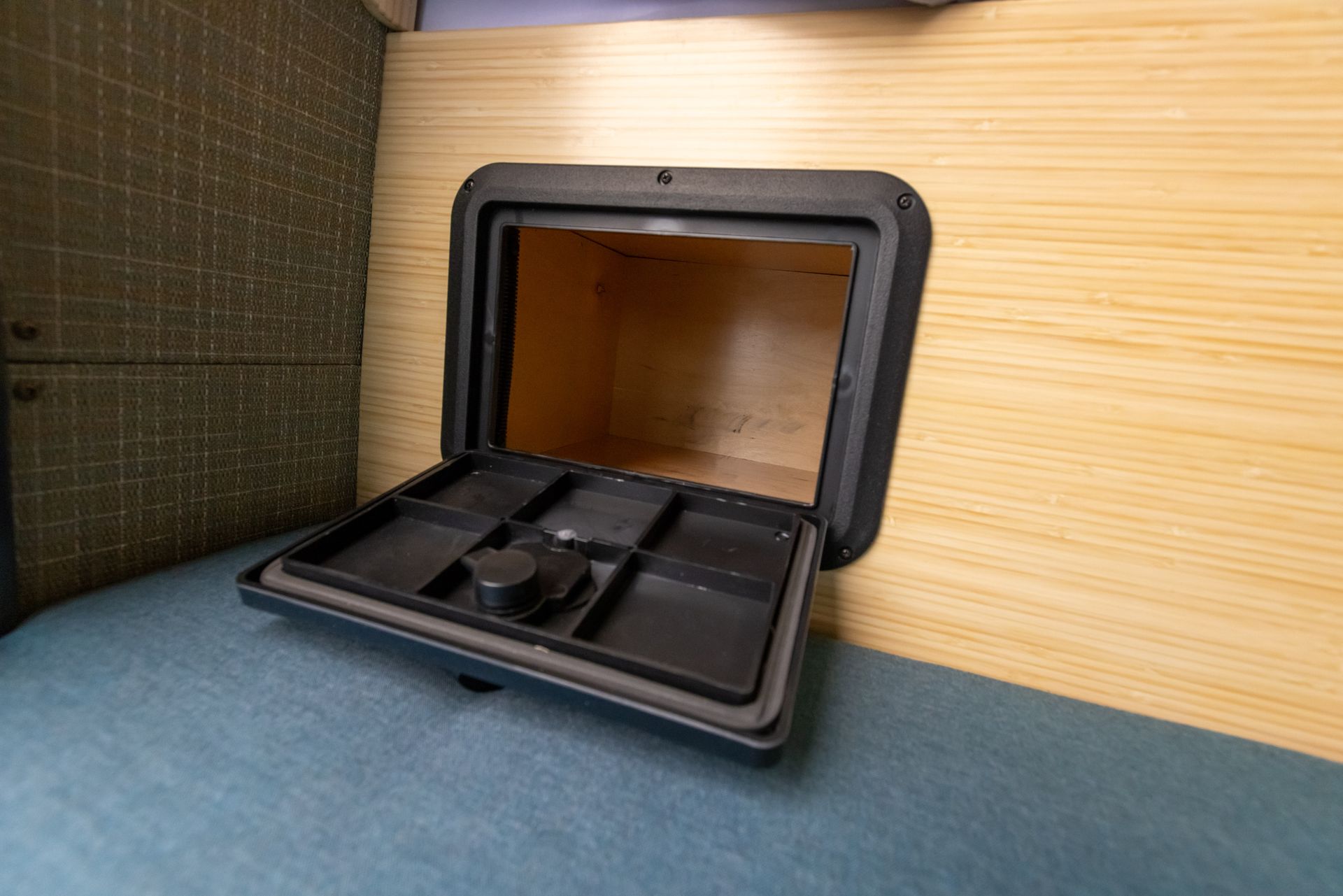 A small black box is sitting on a bed next to a wooden wall.