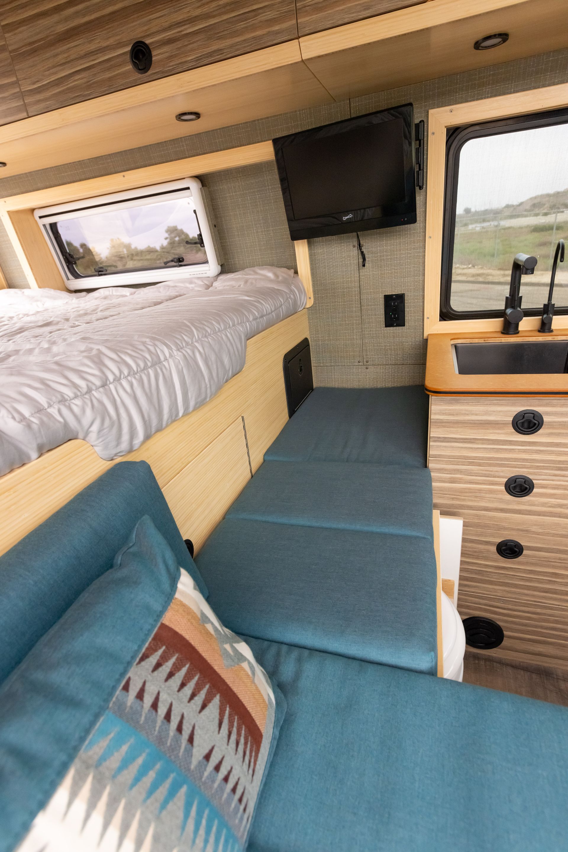 A camper van with a bed , couch , television and sink.