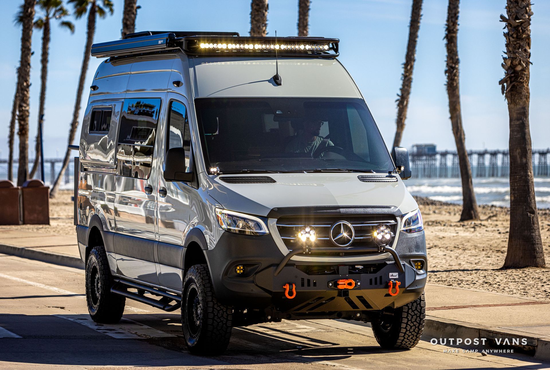 A mercedes sprinter van is parked on the side of the road next to a beach.