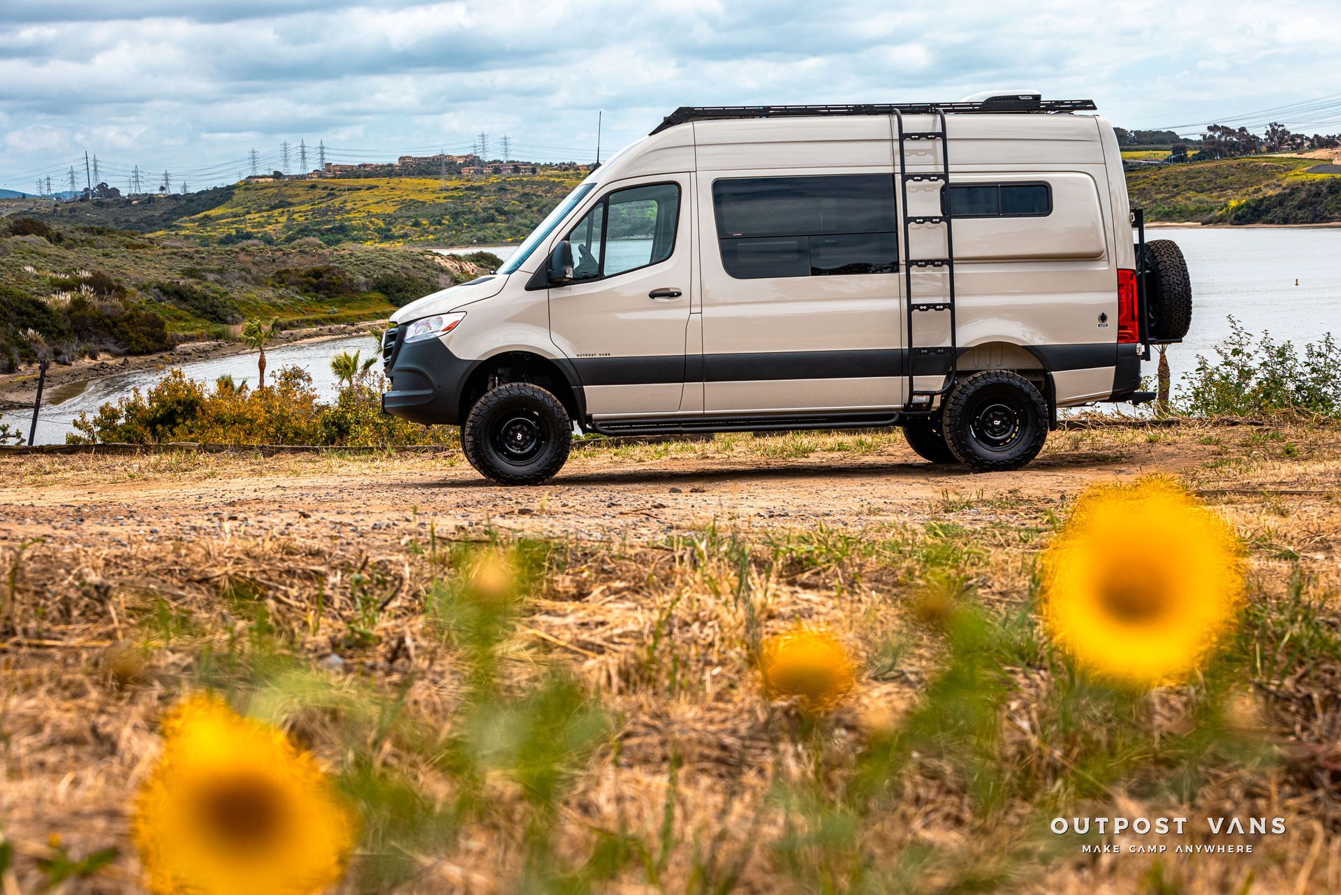 A white van is parked on the side of a dirt road next to a body of water.