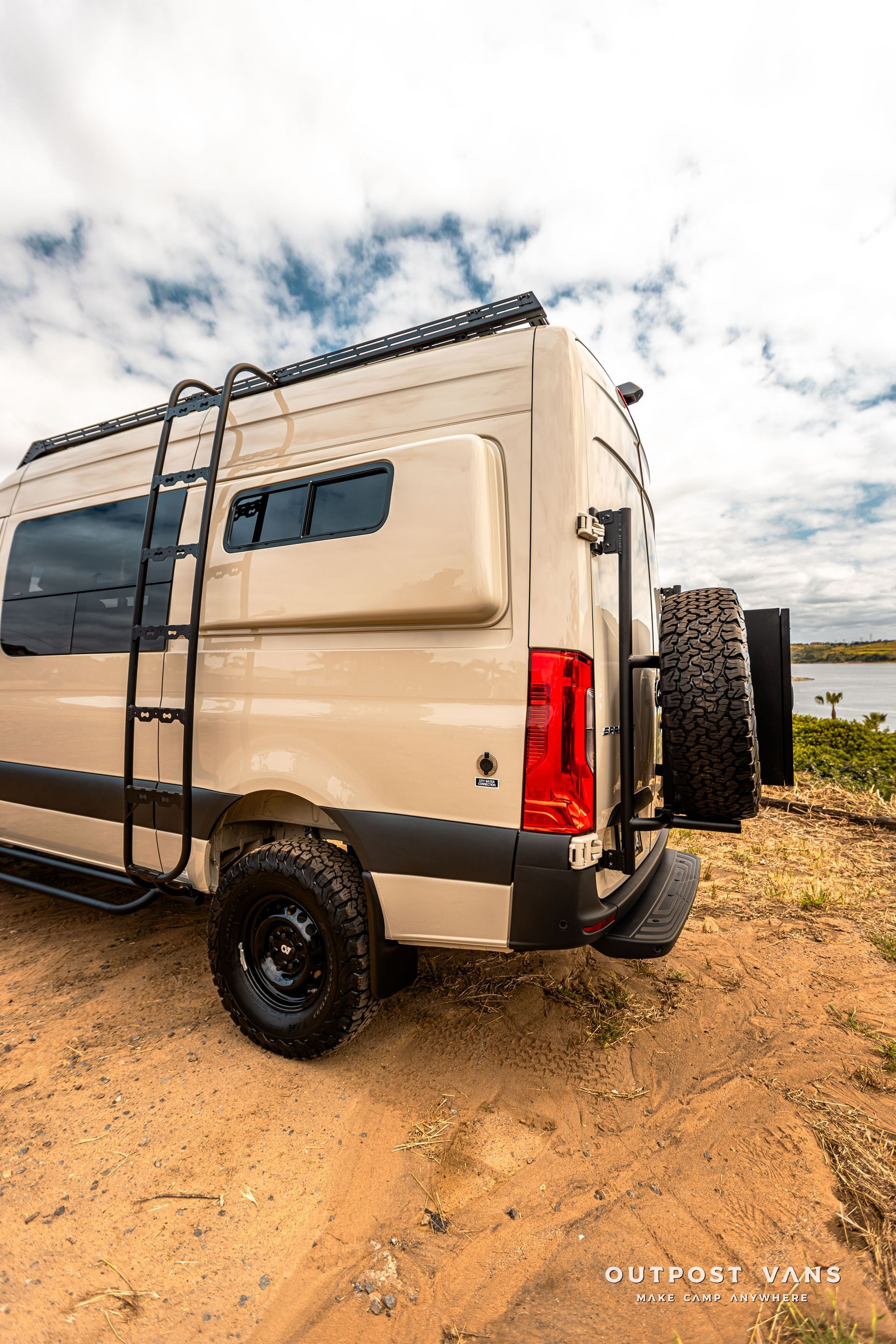 A white van with a ladder on the back is parked on a dirt road.