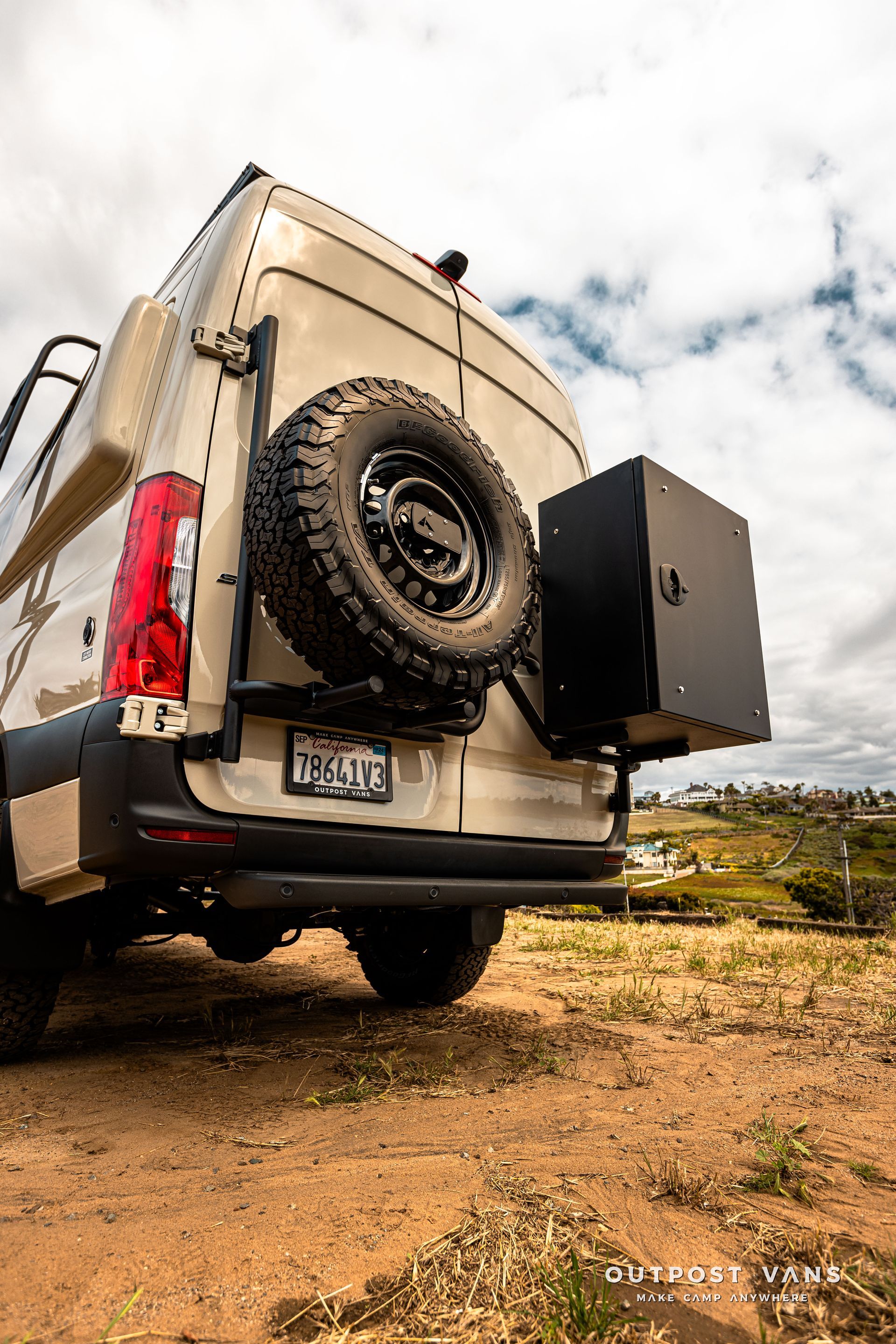 A van with a spare tire attached to the back is parked in a dirt field.