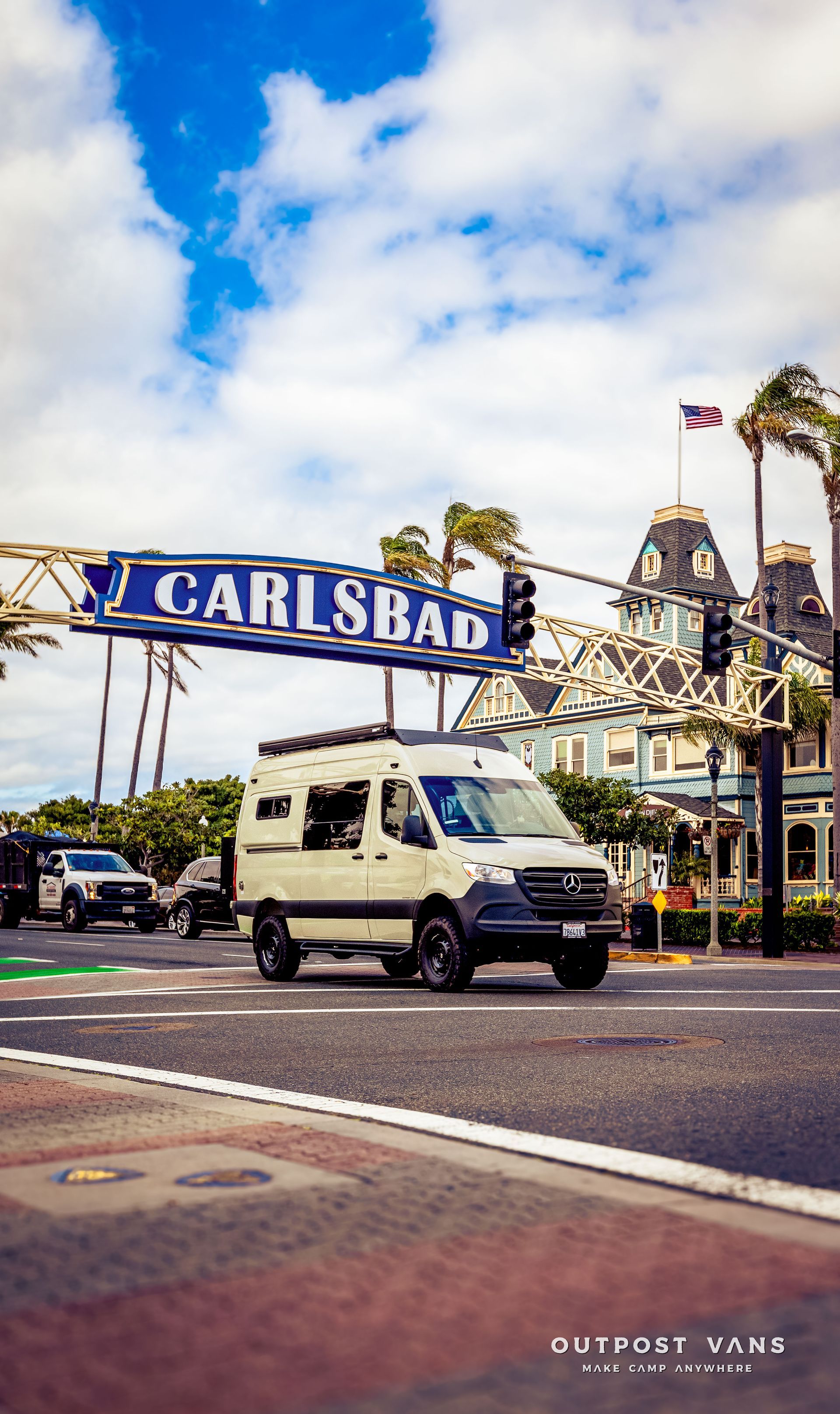 A white van is driving down a street in front of a carlsbad sign.