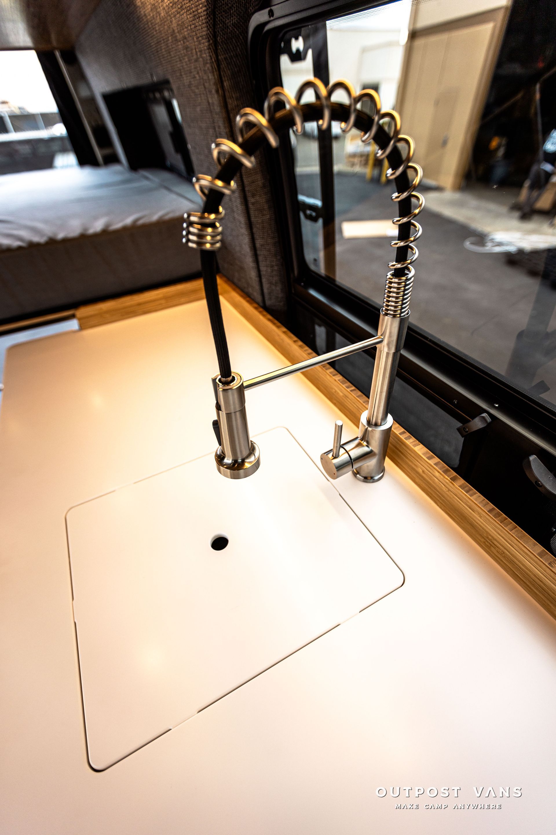 A kitchen sink with a faucet and a window in a camper van.