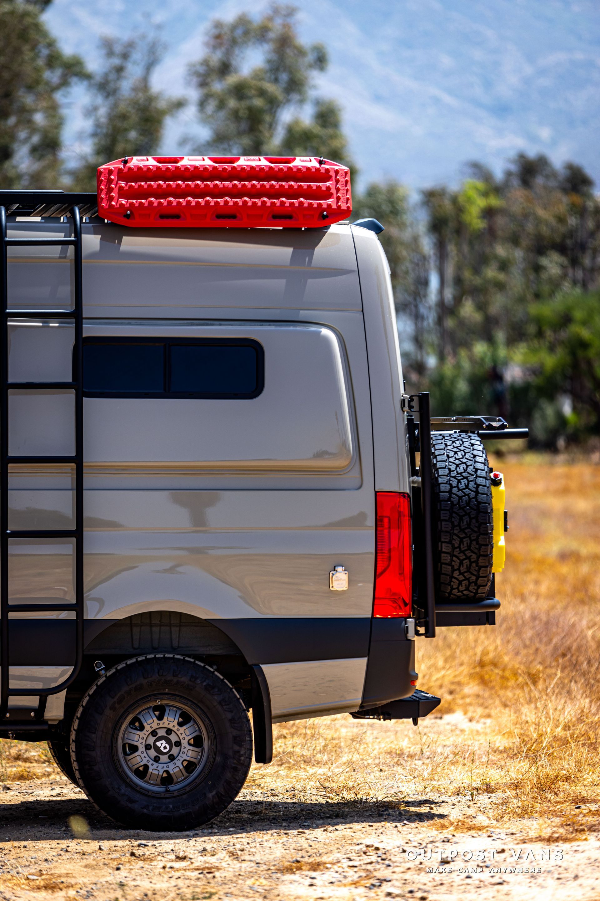 A van with a ladder on the side is parked in a field.