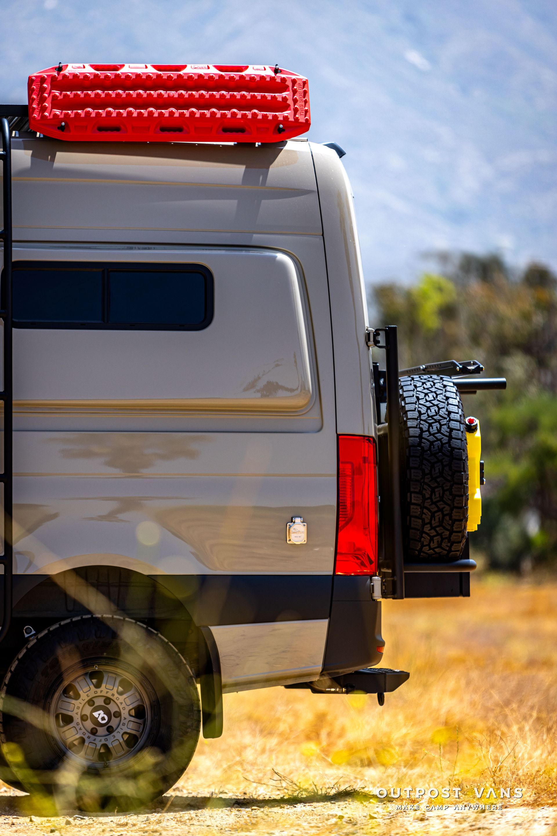 A van with a ladder on the back is parked in a field.