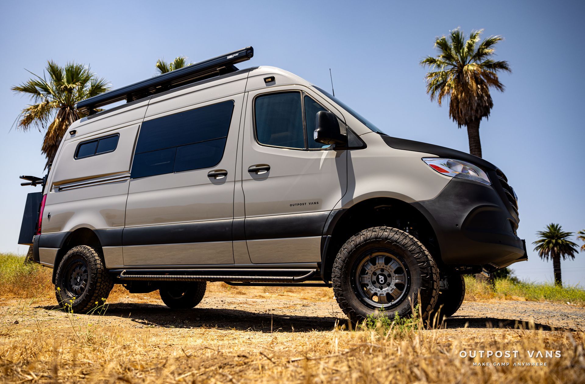 A van is parked in a field with palm trees in the background.