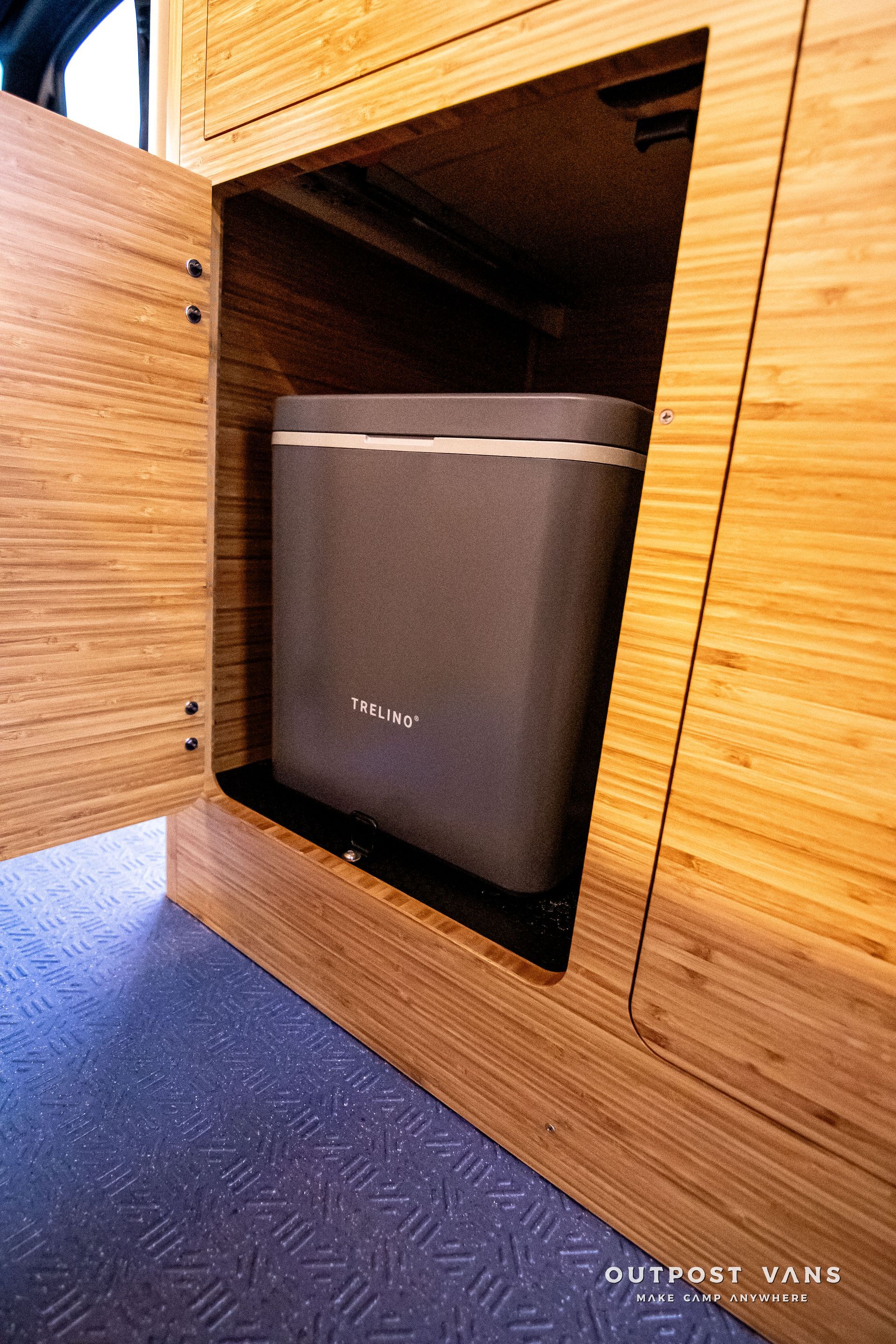 A trash can is sitting inside of a wooden cabinet.